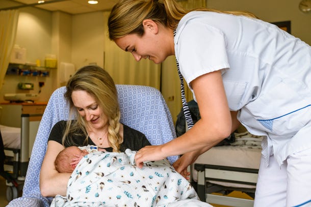 Een moeder met een baby op schoot wordt geholpen door een verpleegkundige.