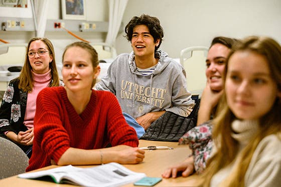 Een groep geneeskundestudenten van de Universiteit Utrecht luistert en lacht tijdens een les, zittend aan een tafel met studiemateriaal