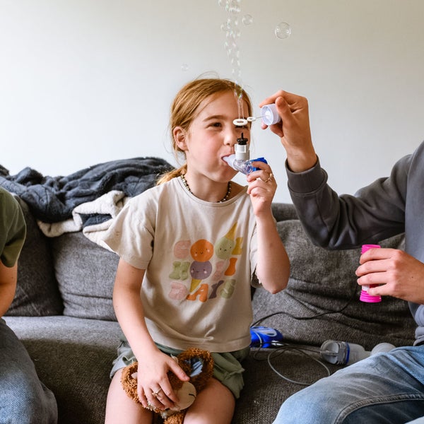 Veerle heeft cystic fibrosis (CF) en neemt medicijnen met een pufje in. Haar broer houdt een bellenblaas boven de uitlaat van het pufje, zodat er bubbels verschijnen.
