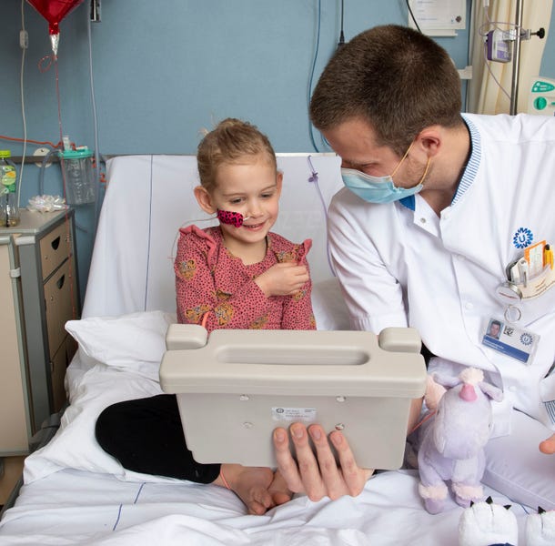 Meisje en zorgverlener zitten op een ziekenhuisbed en kijken naar een tablet.