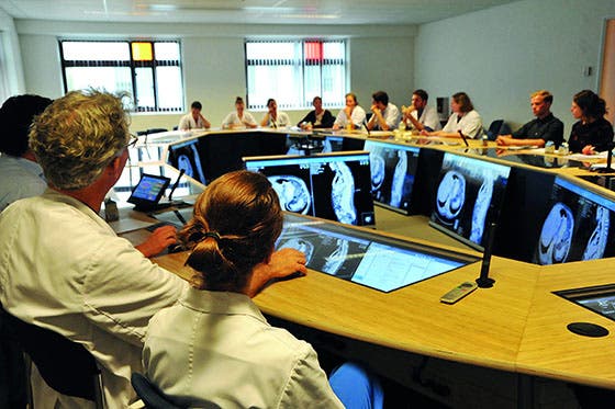 Medisch team in discussie rondom een grote tafel met computerschermen waarop medische beelden worden getoond in een vergaderruimte
