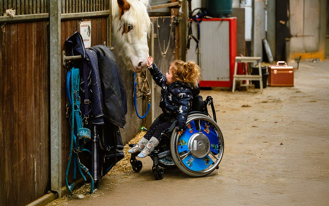 Elena zit in een rolstoel en aait een paard