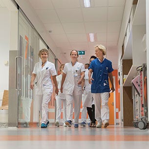 Medisch personeel loopt lachend door de gang van een ziekenhuis, gekleed in witte en blauwe uniformen, in het UMC Utrecht