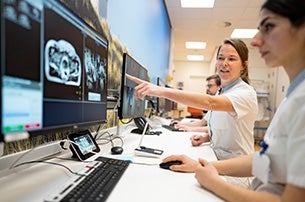 Medische professionals in witte jassen bekijken en bespreken röntgenbeelden op computerschermen in een kantoor van het UMC Utrecht