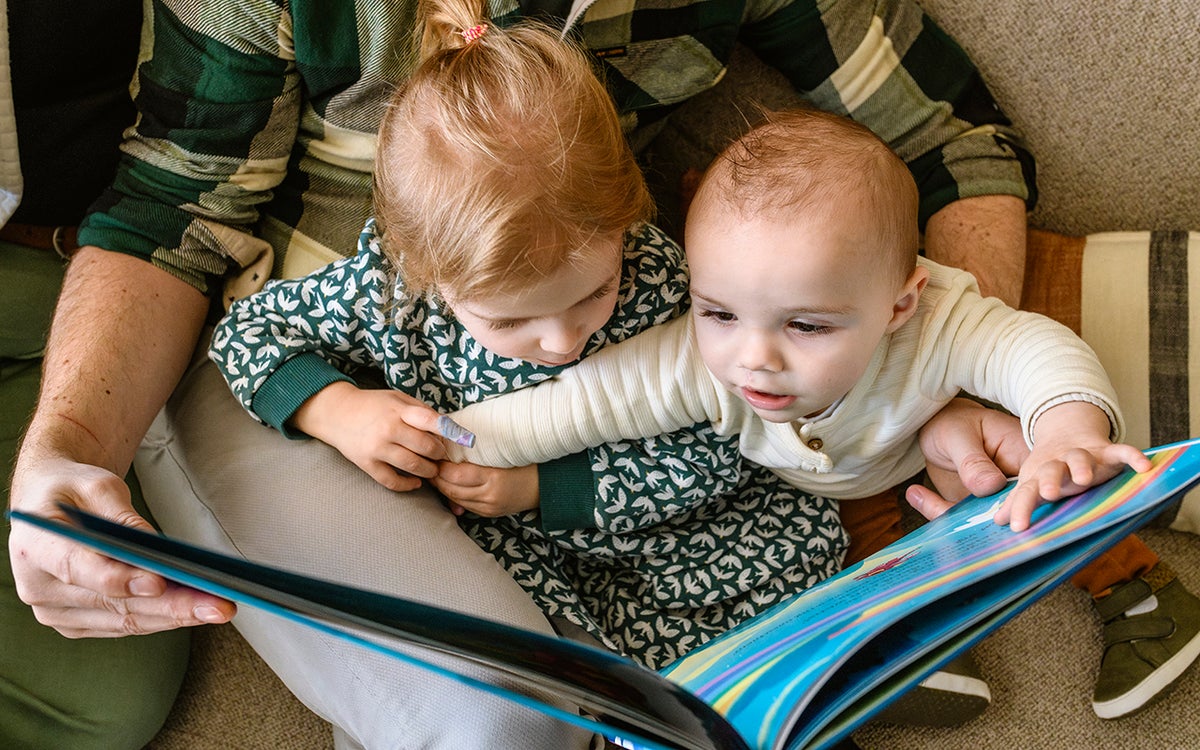 Emma en Thomas lezen een boekje bij hun vader op schoot