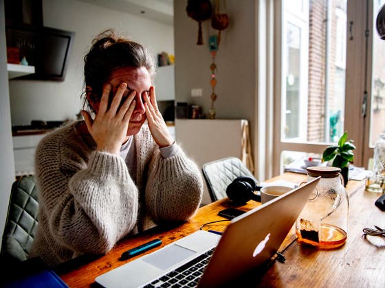 Een vrouw zit met haar handen tegen haar hoofd voor een laptop