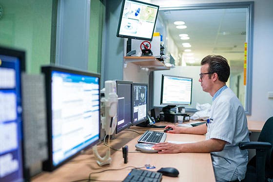 Een arts werkt geconcentreerd achter meerdere computerschermen in een controlekamer, analyserend medische gegevens en beelden voor prostaatkankeronderzoek