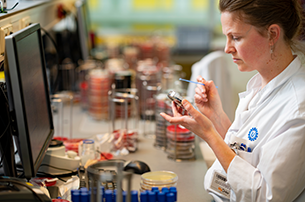Laboratoriummedewerker in witte jas onderzoekt monsters in een laboratorium met petrischalen en apparatuur op de achtergrond, UMC Utrecht