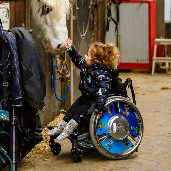 Elena zit in een rolstoel en aait een paard