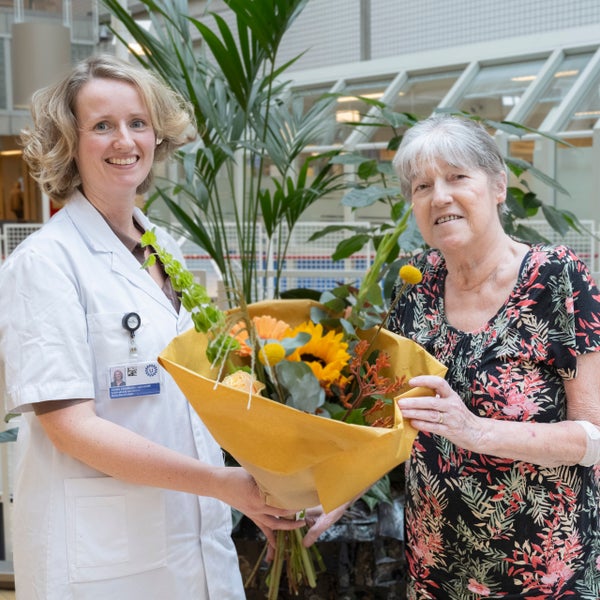 Een zorgverlener overhandigt een patiënt een boeket bloemen omdat de patiënt de 600e longtransplantatie heeft ondergaan.