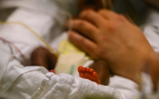 A small baby in a bed with an adult hand tending to the baby 