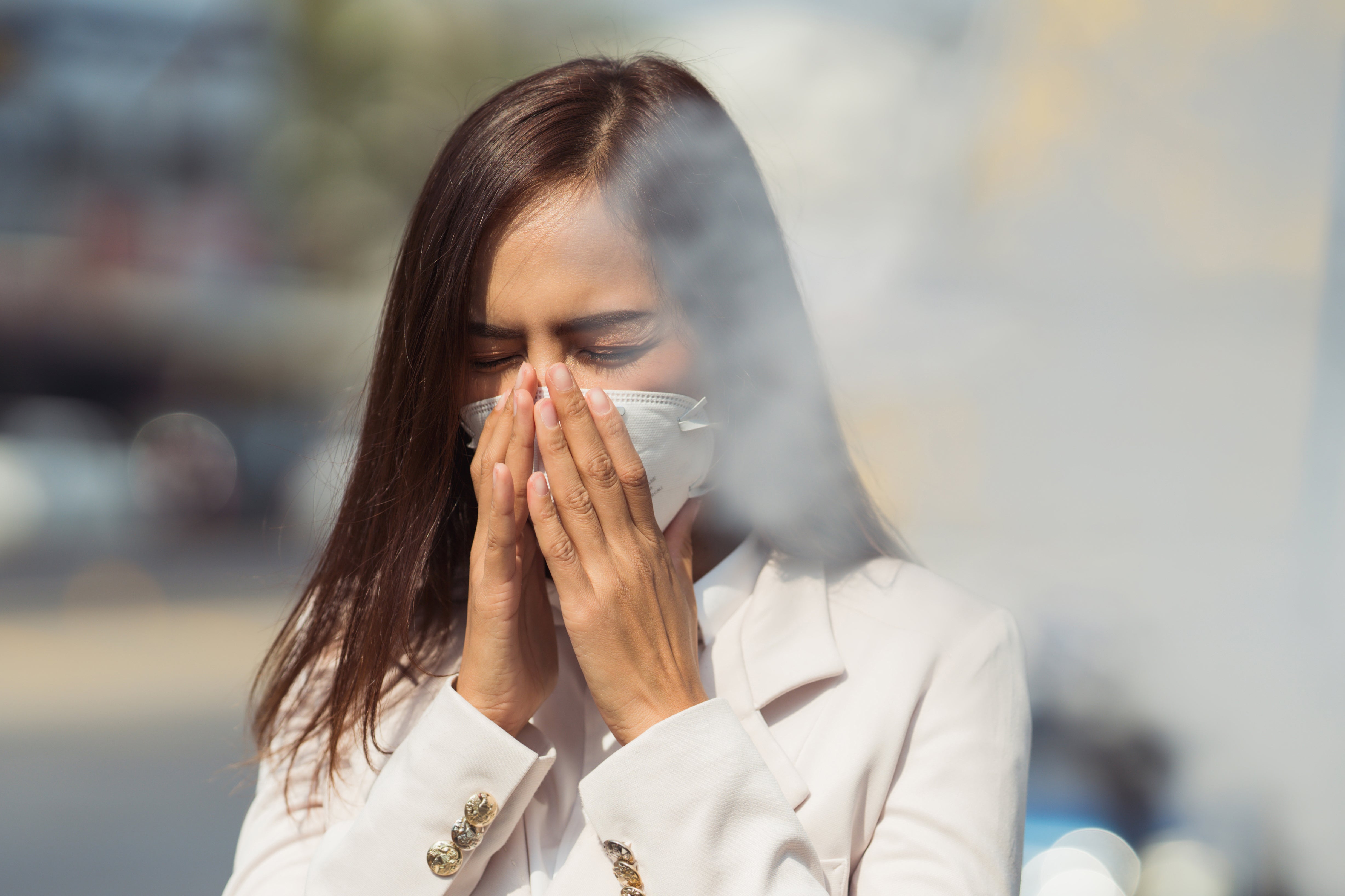 Vrouw met mondkapje op loopt door rook heen. Luchtvervuiling raakt vaker Nederlanders met een migratieachtergrond.