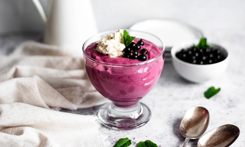 A glass bowl of blackcurrant mouse with blackcurrants cream and two mint leaves on top