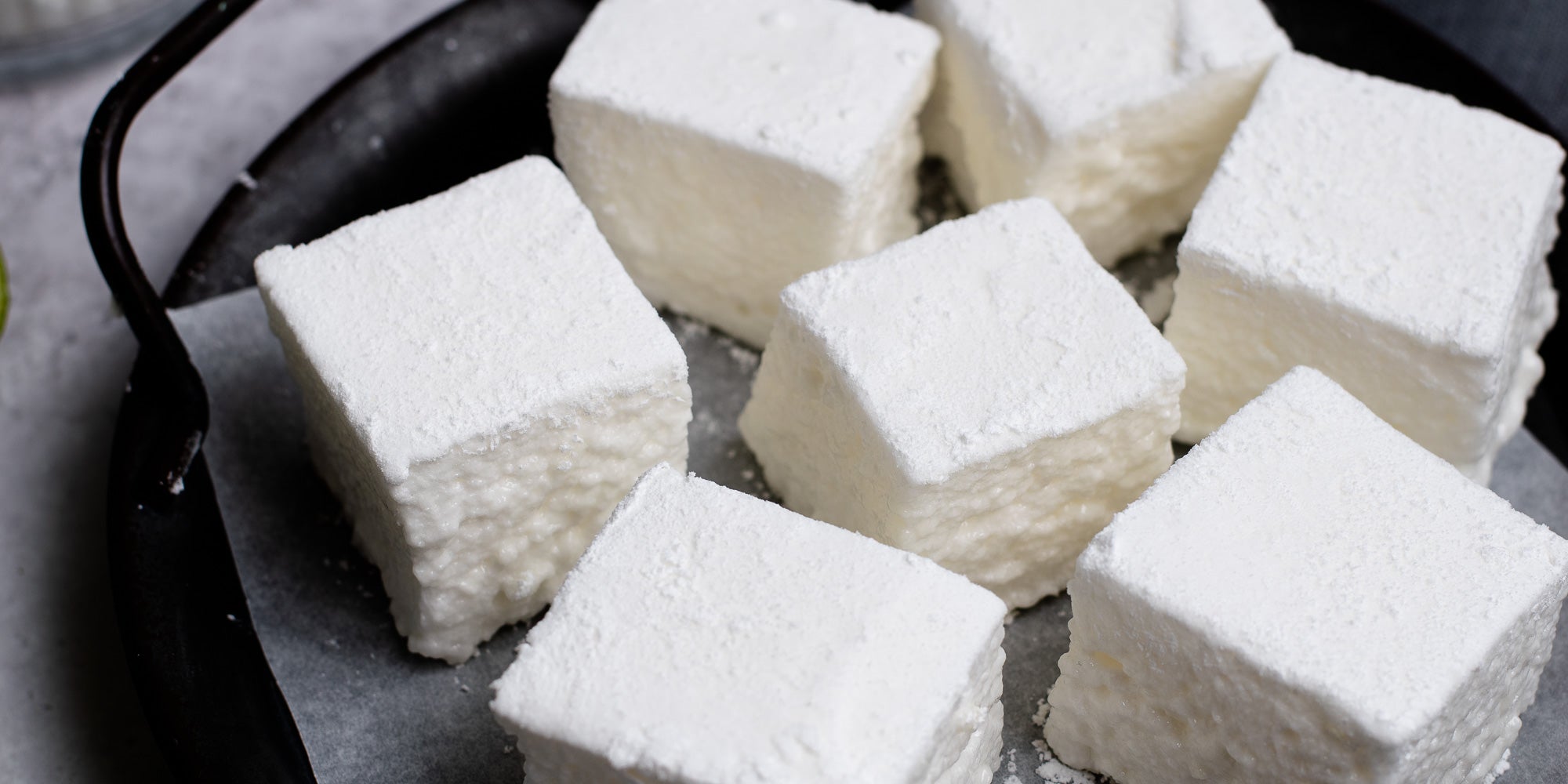 Gin & Tonic Marshmallows on baking paper on a black tray dusted with icing sugar