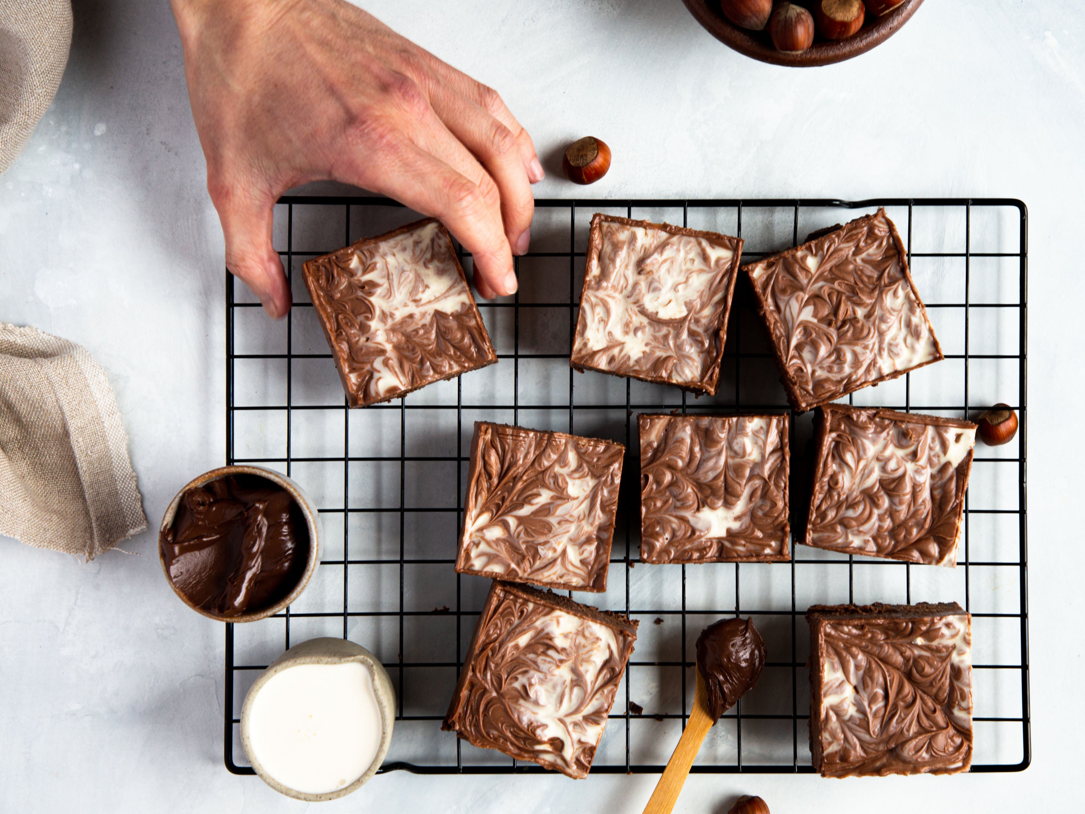 Nutella Cheesecake Bars on a wire cooling rack with a hand reaching to take a piece