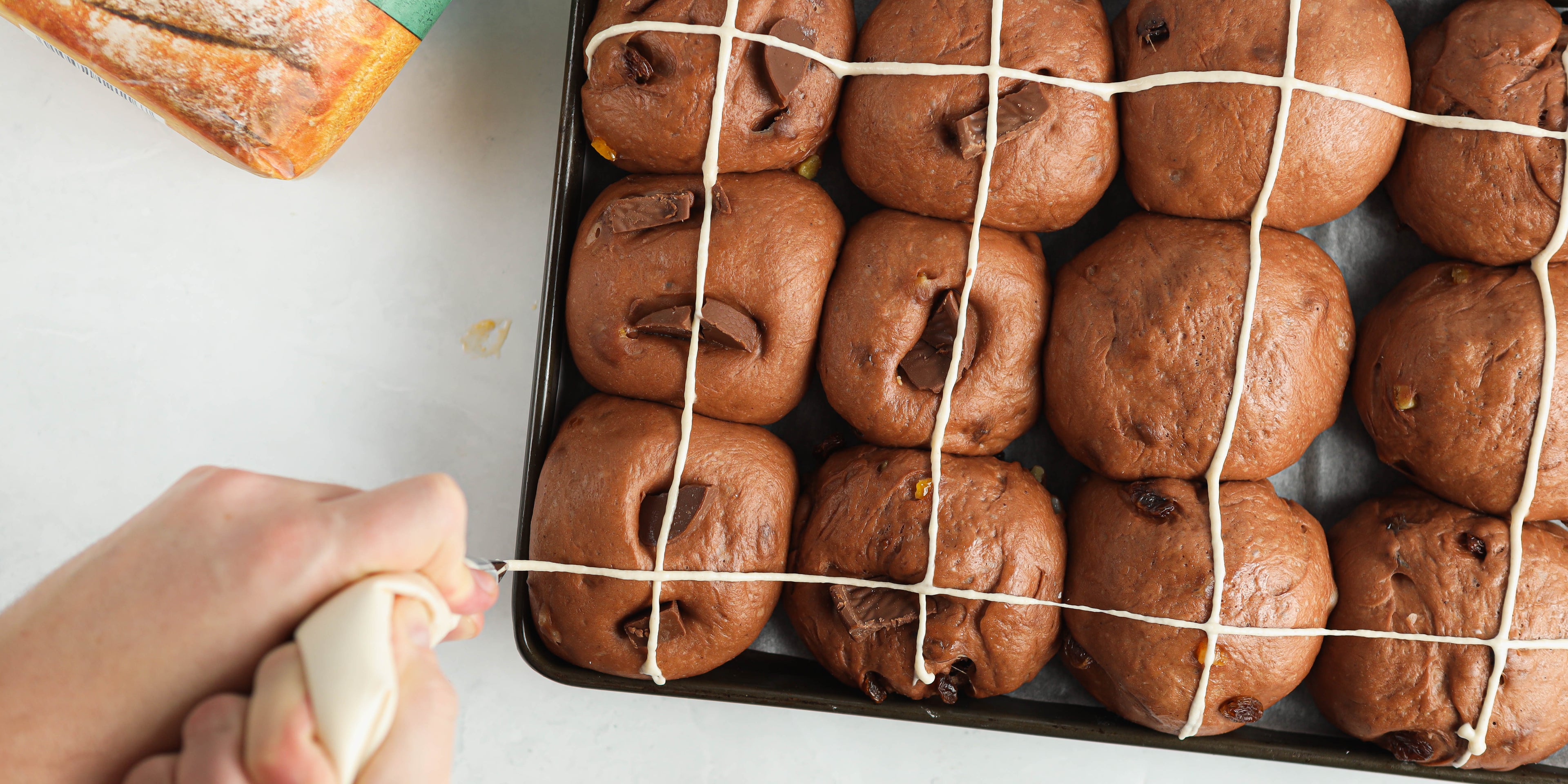 Piping white crosses onto chocolate hot cross buns