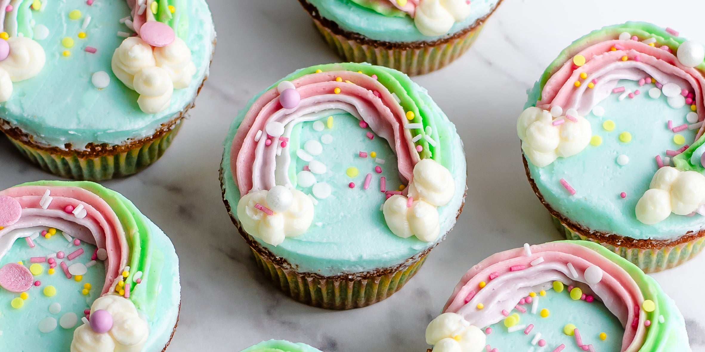 Close up on several cupcakes decorated with blue buttercream and a rainbow decoration