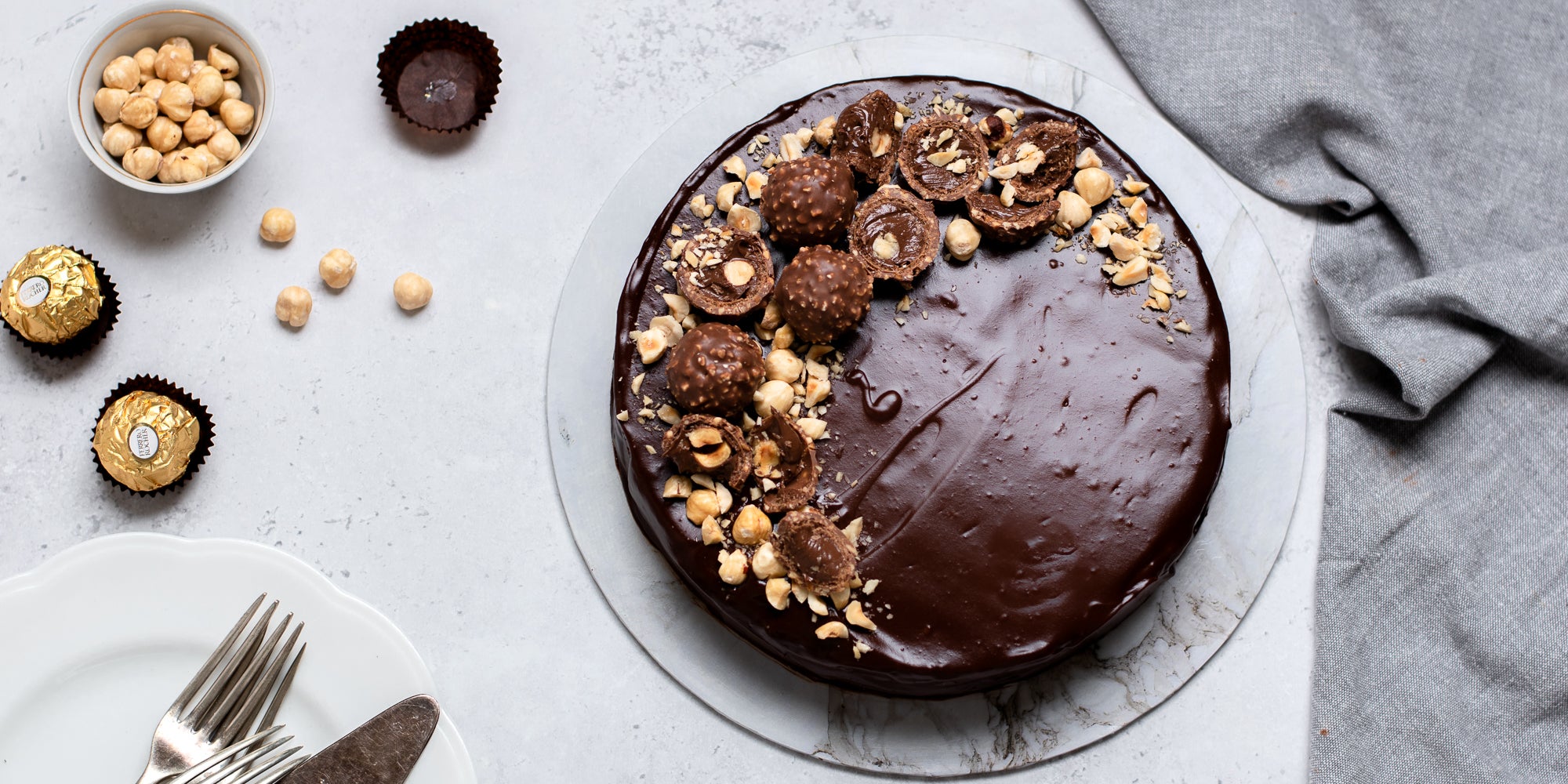 Top view of Gluten Free Chocolate Truffle Sachertorte next to a bowl of hazelnuts, and Ferrero Rocher's. Topped with chopped nuts.