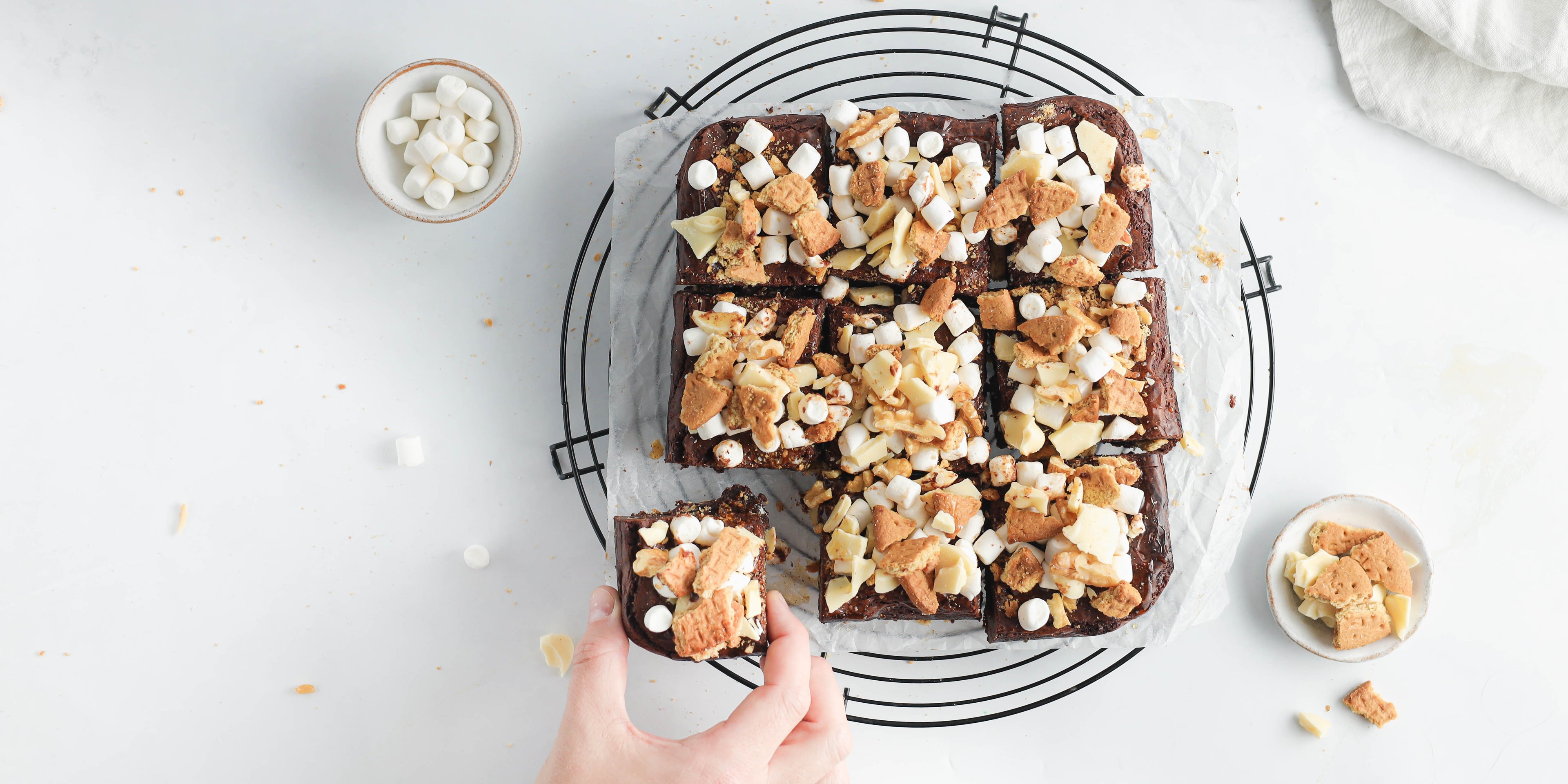 Top view of Rocky Road Brownies cut into squares topped with marshmallows with a hand reaching for a slice