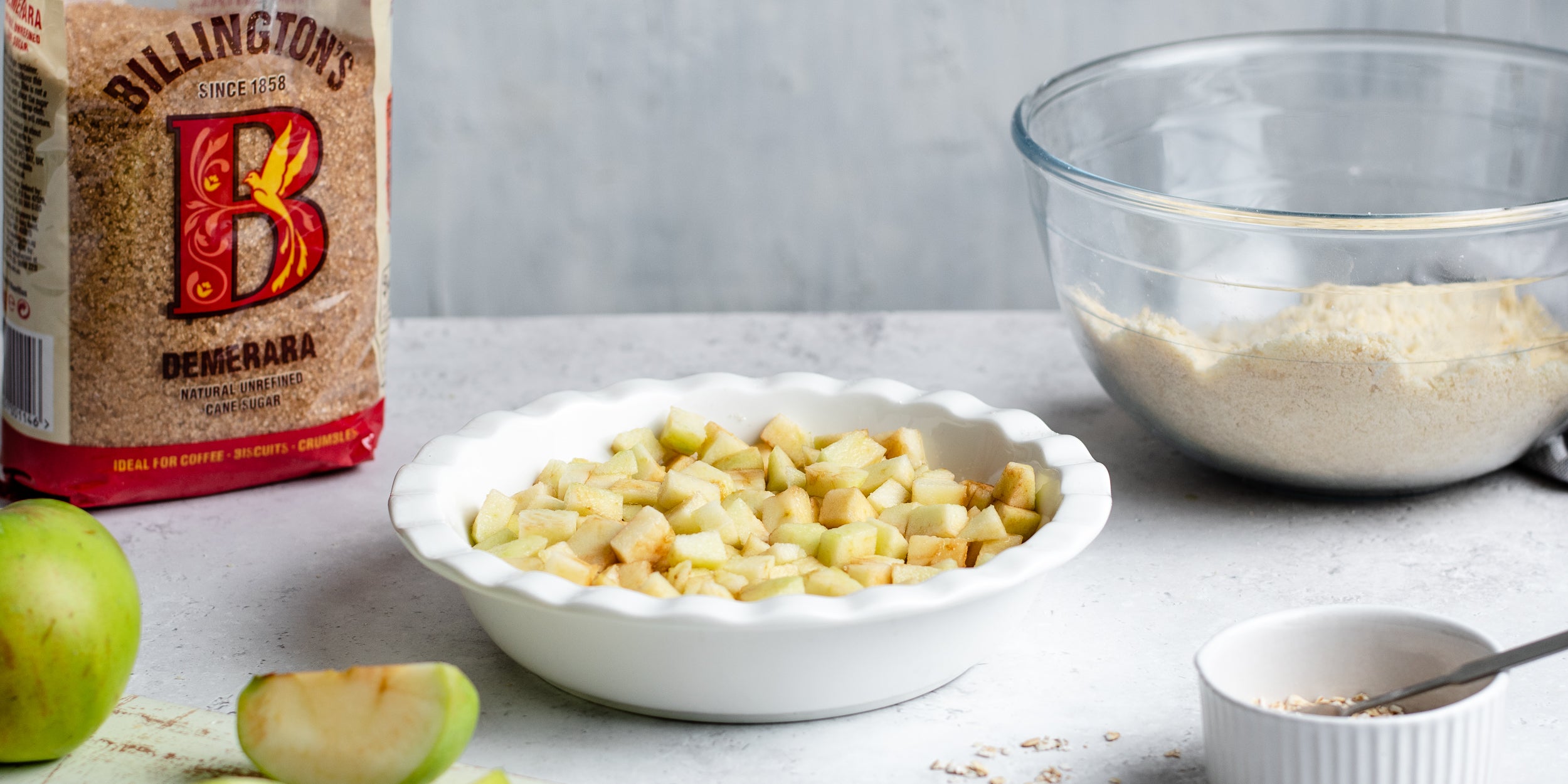 Chopped apples ready to bake for the base of the Ultimate Apple Crumble next to a bag of Billington's Demerara sugar and crumble to sprinkle on top