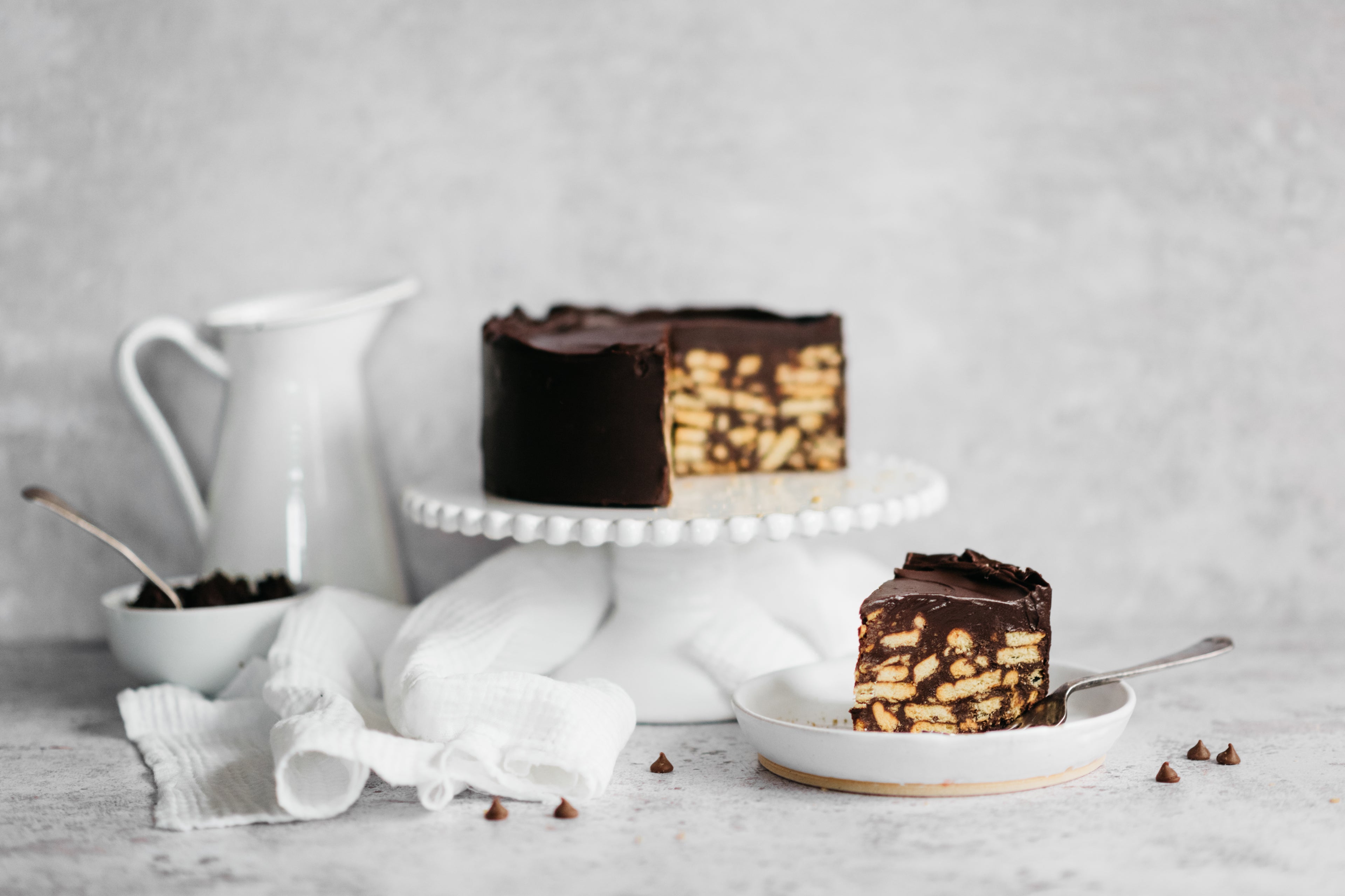 Chocolate Biscuit Cake on a cake stand with a slice cut out showing the rich tea biscuits inside