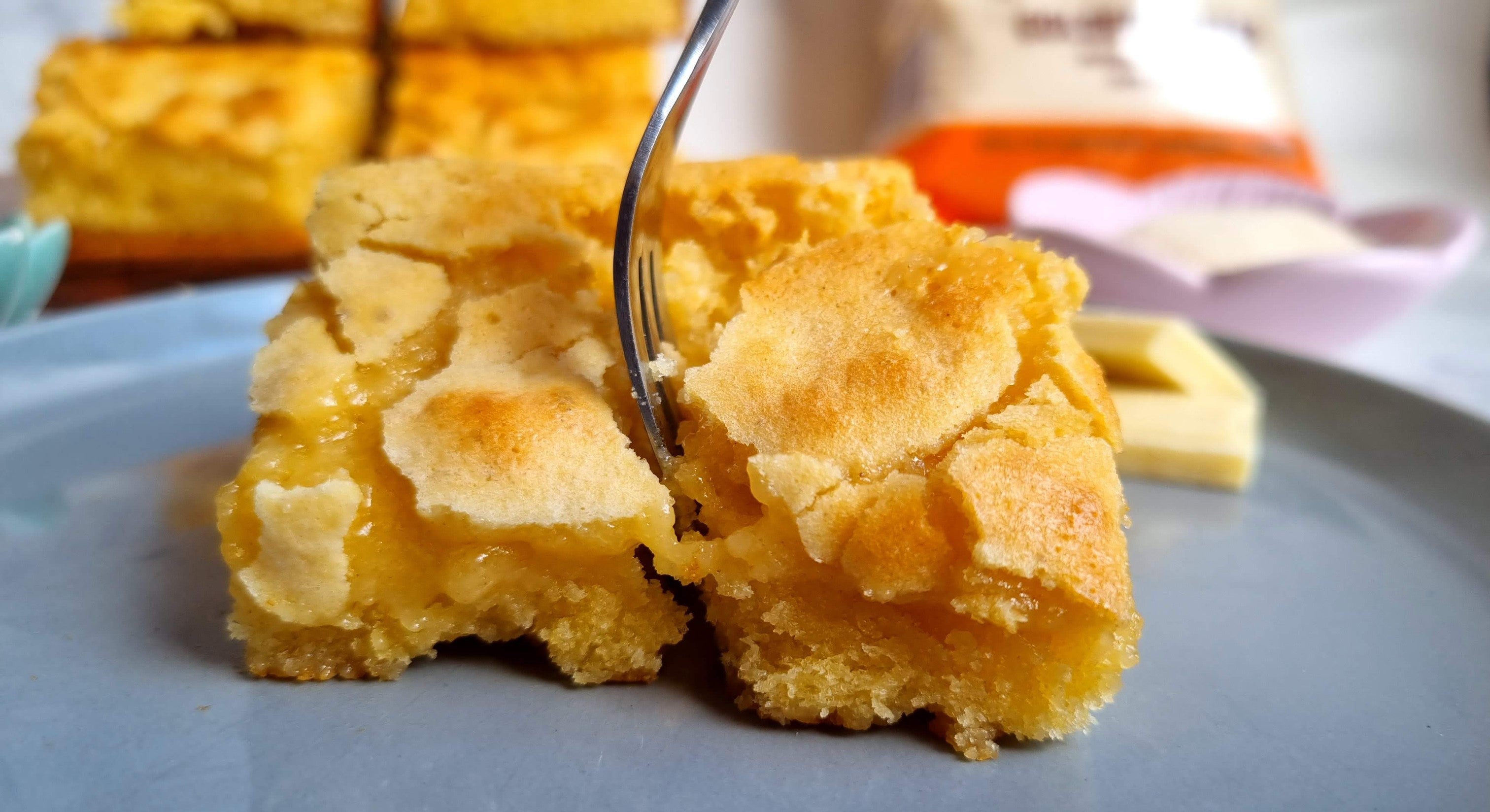 White chocolate brownies with a crisp papery topping being cut into with a fork