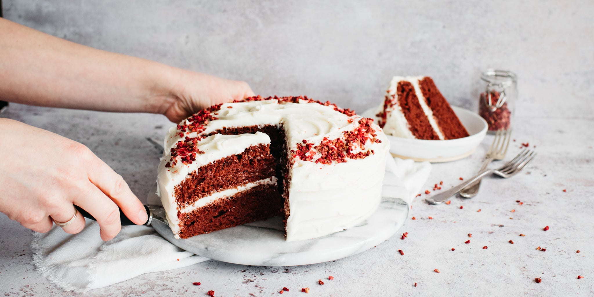 Hand reaching for a slice of Red Velvet Cake using a cake knife to serve