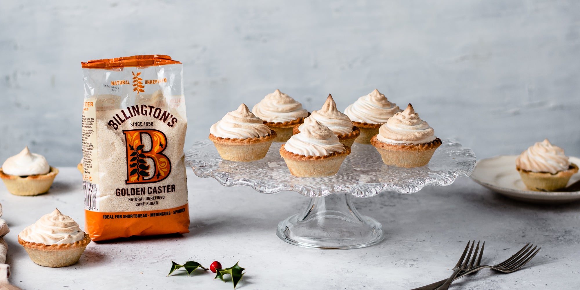 Meringue Topped Mince Pies on a glass cake stand next to a bag of Billington's Golden caster sugar