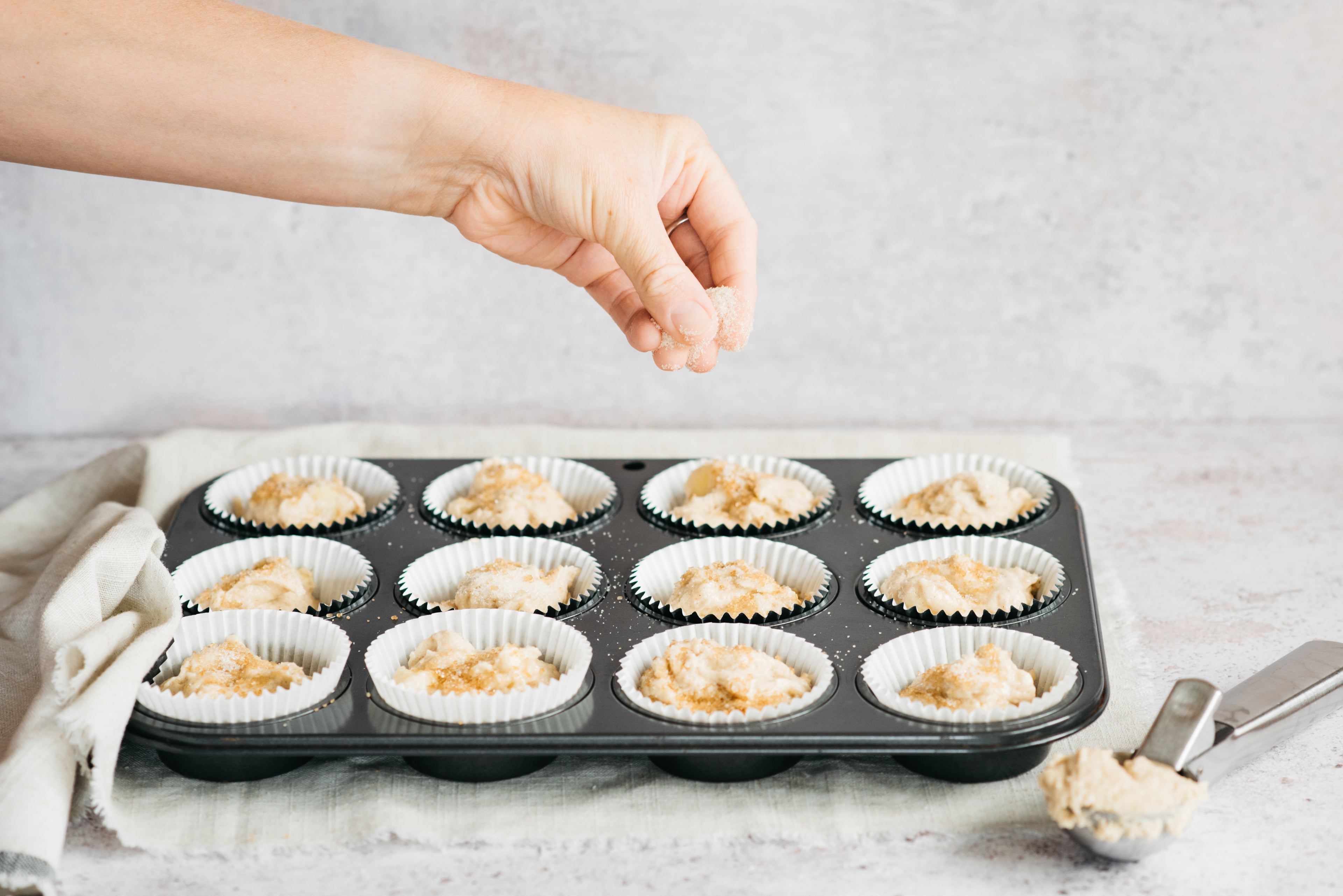 Hand sprinkling sugar on top of muffins in baking tray