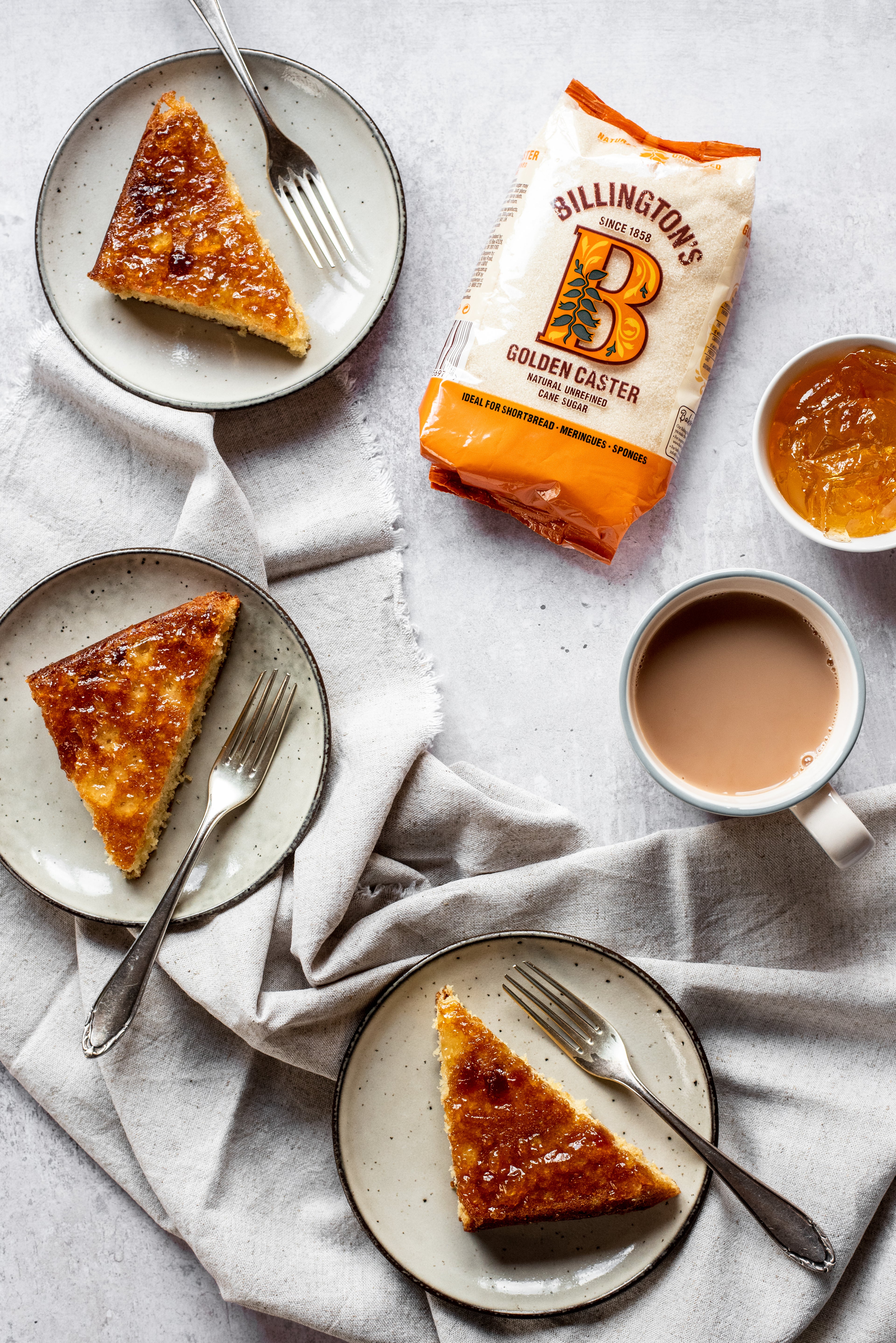 Slices of Marmalade Traybake on plates served with forks, next to a bag of Billington's Caster Sugar and a bowl of marmalade