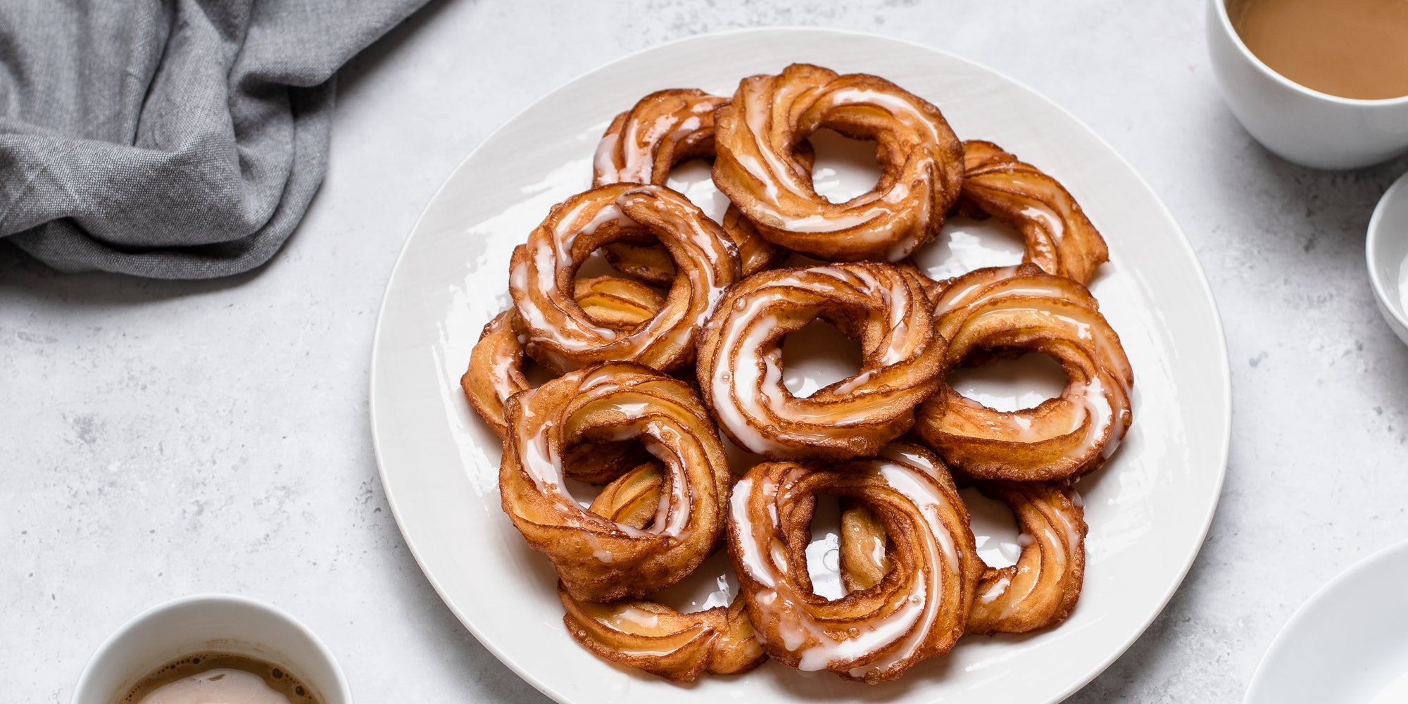 Close up of a plate of Apple Cider Crullers with icing and cinnamon sprinkled ontop