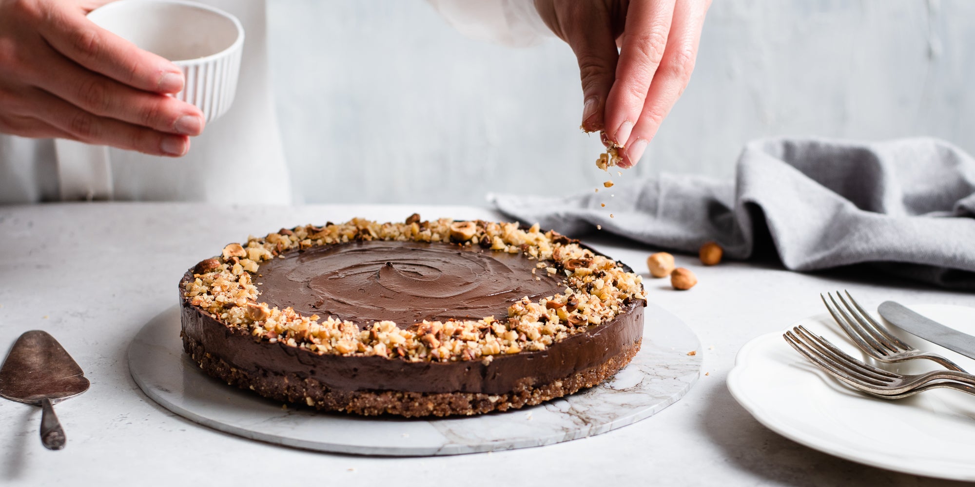 Raw Chocolate Avocado Cheesecake being hand finished with with chopped nuts by a hand from above