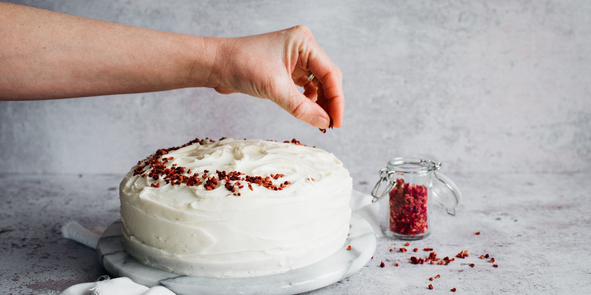 Hands sprinkling decorations on the buttercream icing of a red velvet cake
