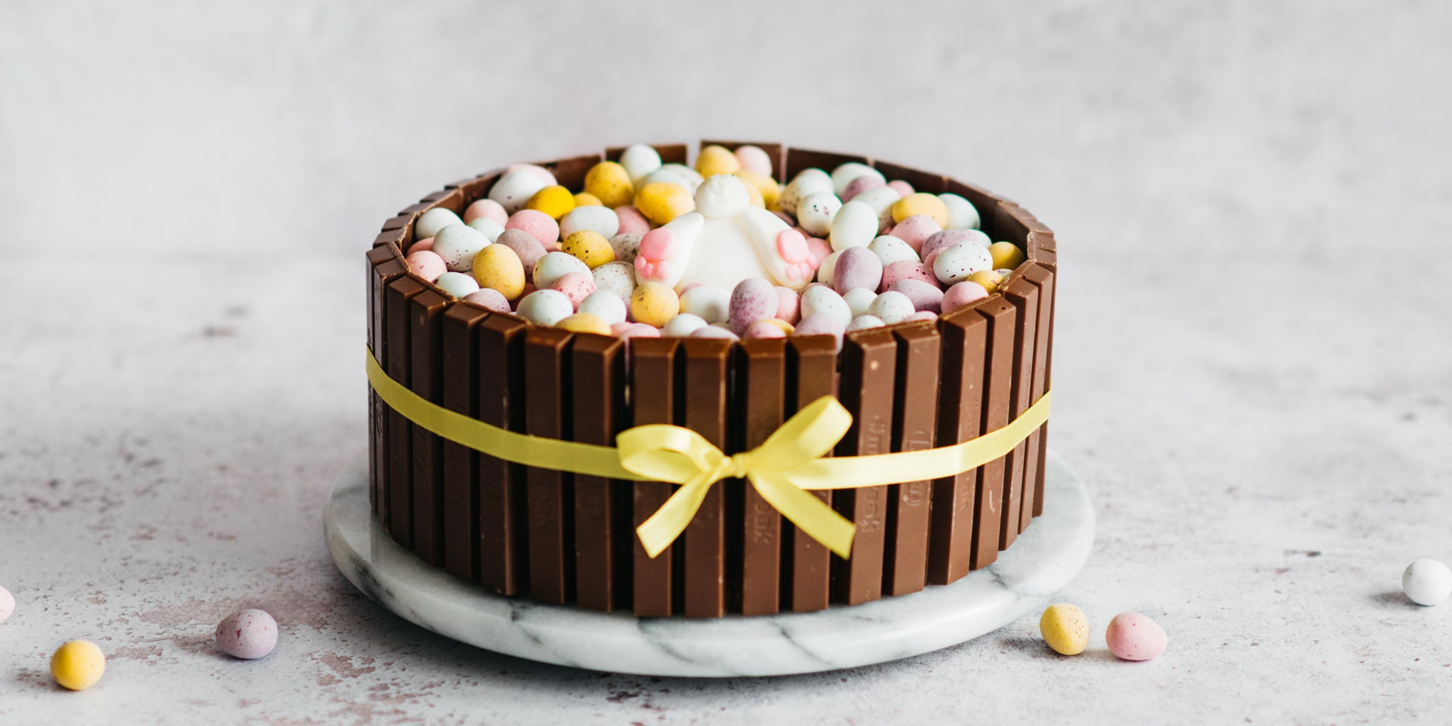 Cake decorated in kit kats and yellow ribbon with mini eggs in the foreground