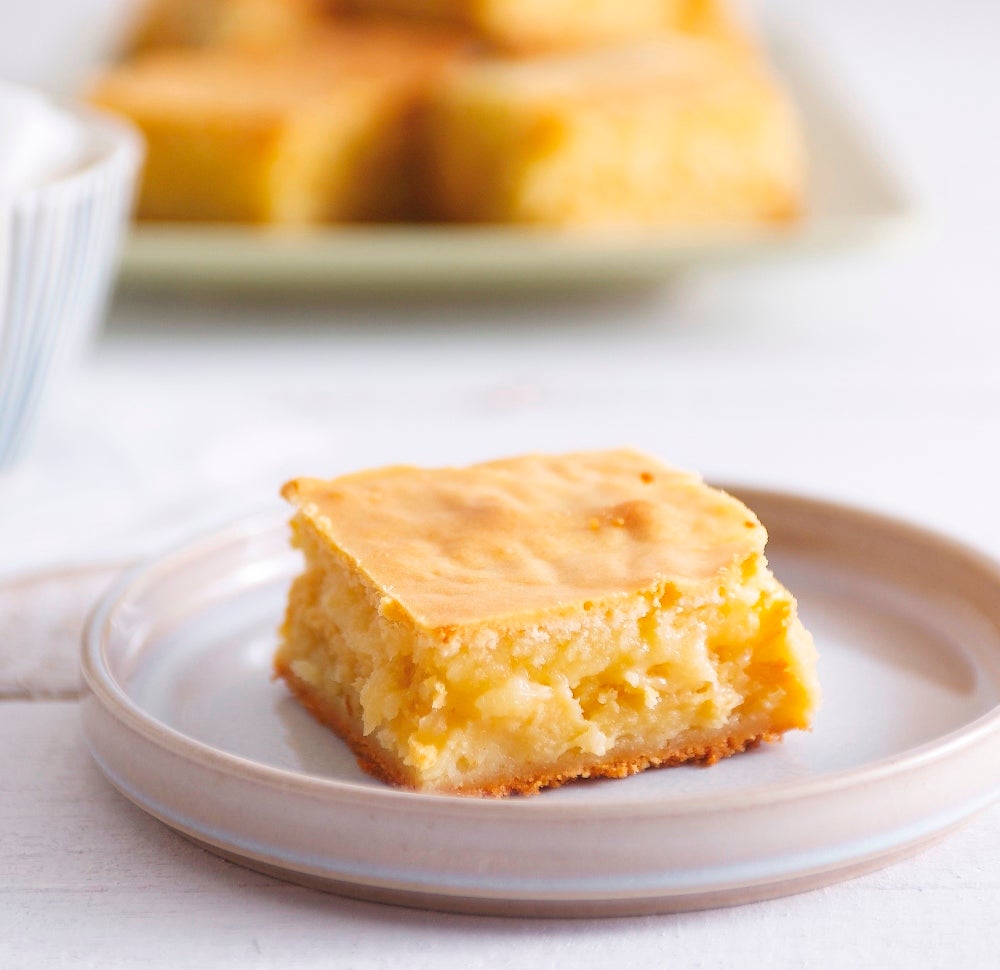 Freshly-baked white chocolate blondie sitting on a pale terracotta plate