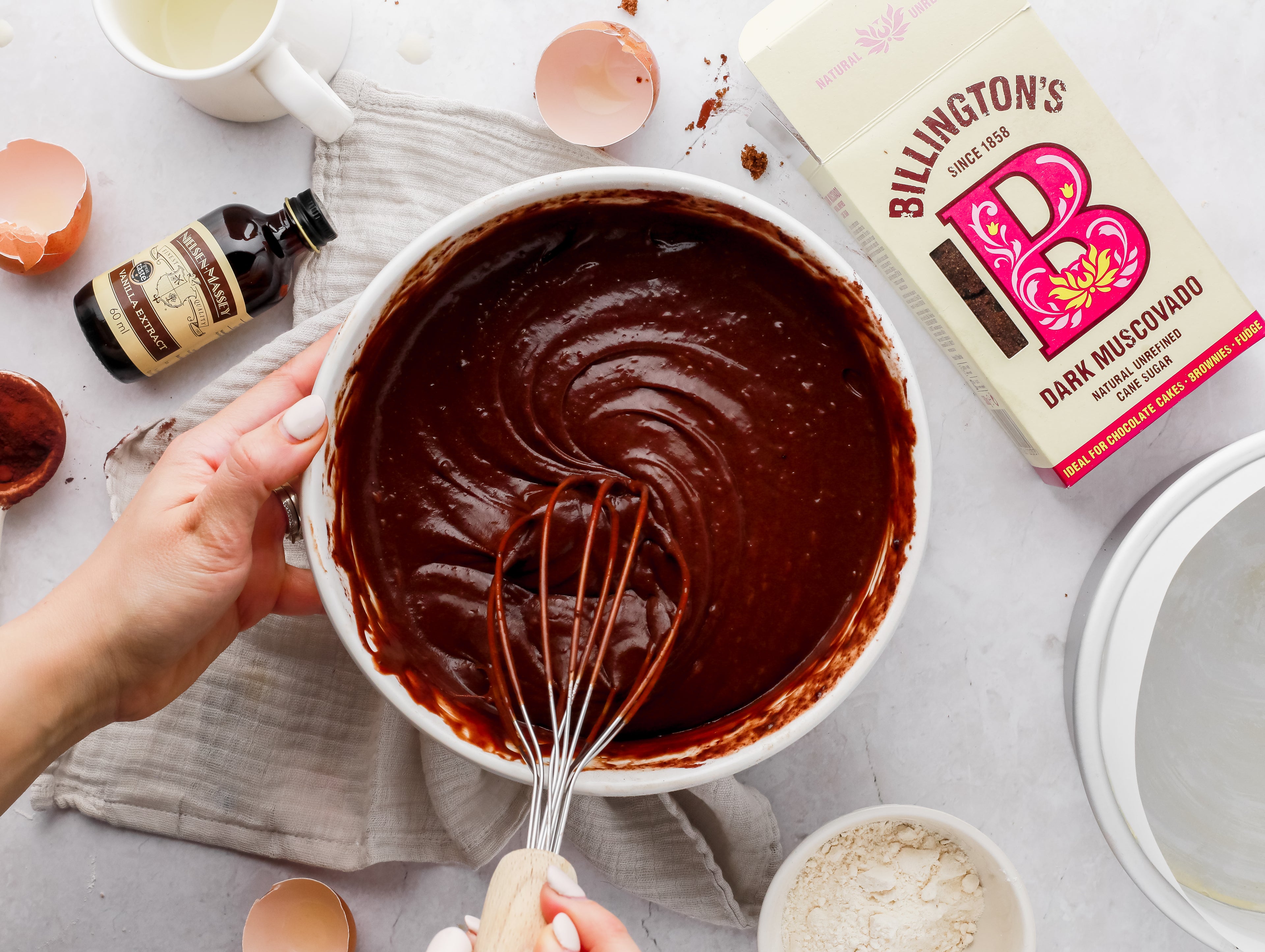 Chocolate cake mix being whisked in a bowl surrounded by baking ingredients