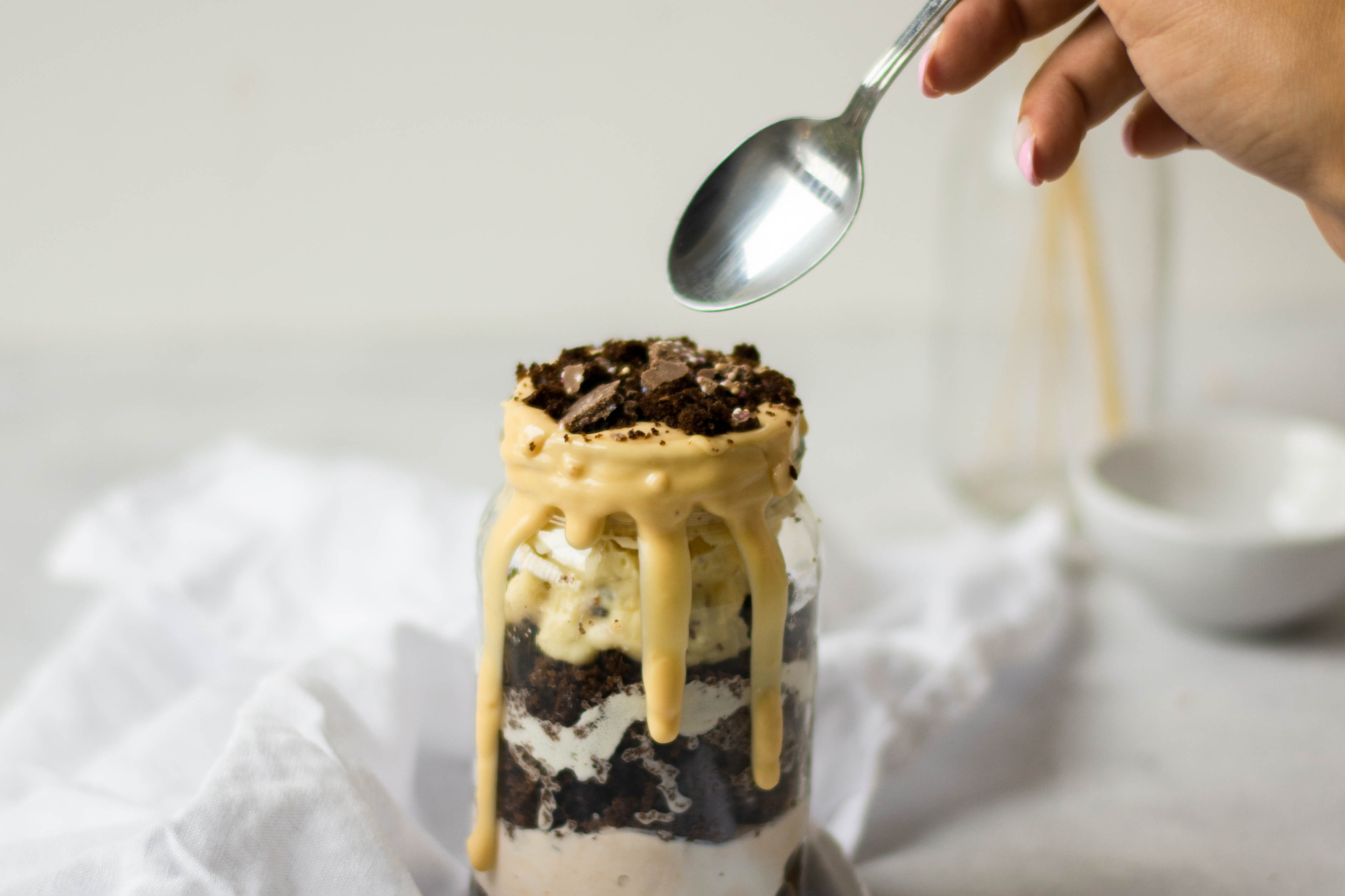 Close up of Baileys Cake Jar with topping dripping down the sides. A hand holding a spoon ready to dip into the jar.