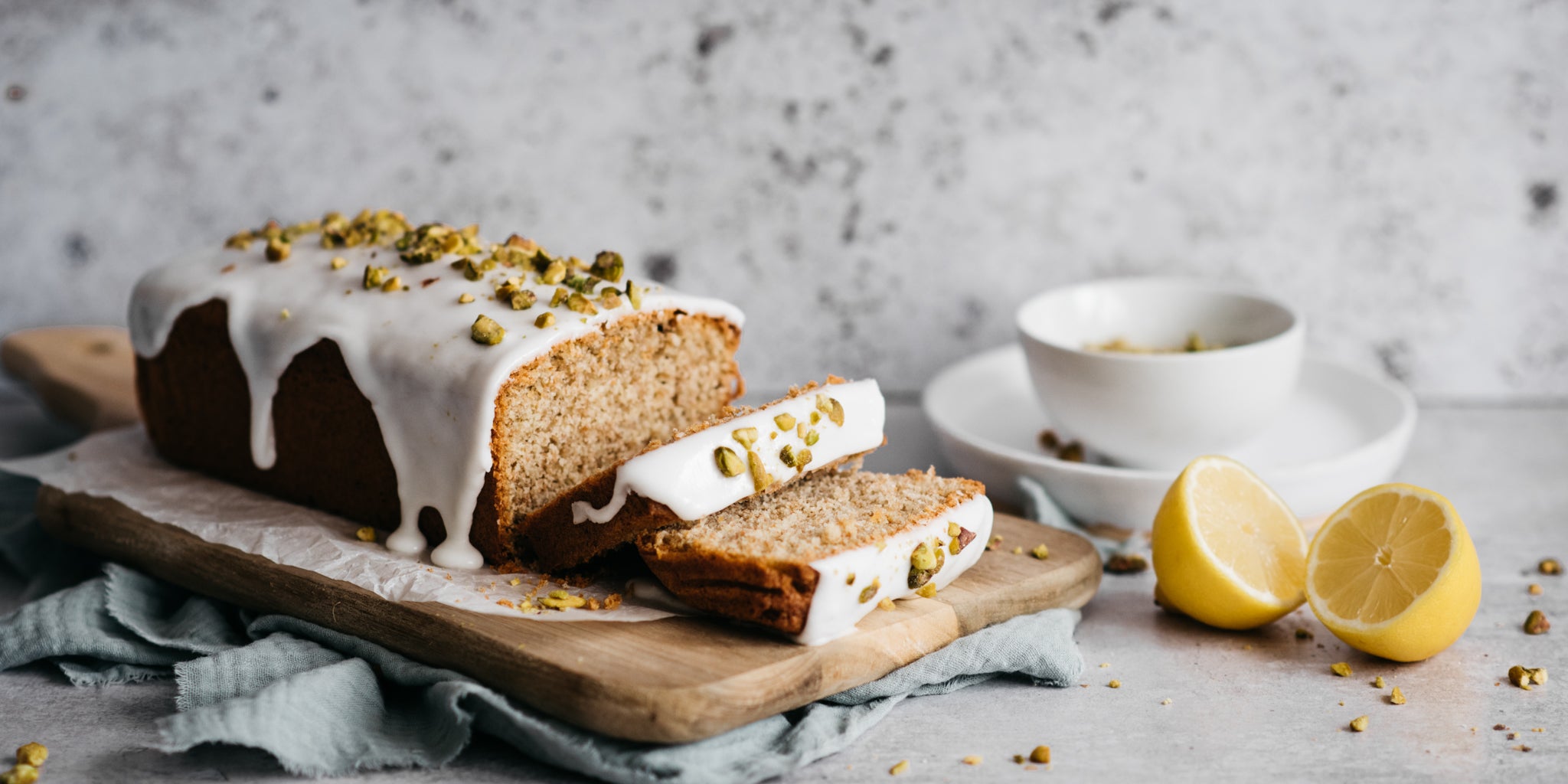 Gluten Free Vegan Lemon Drizzle Cake sliced into pieces next to a lemon cut in half and ground nuts