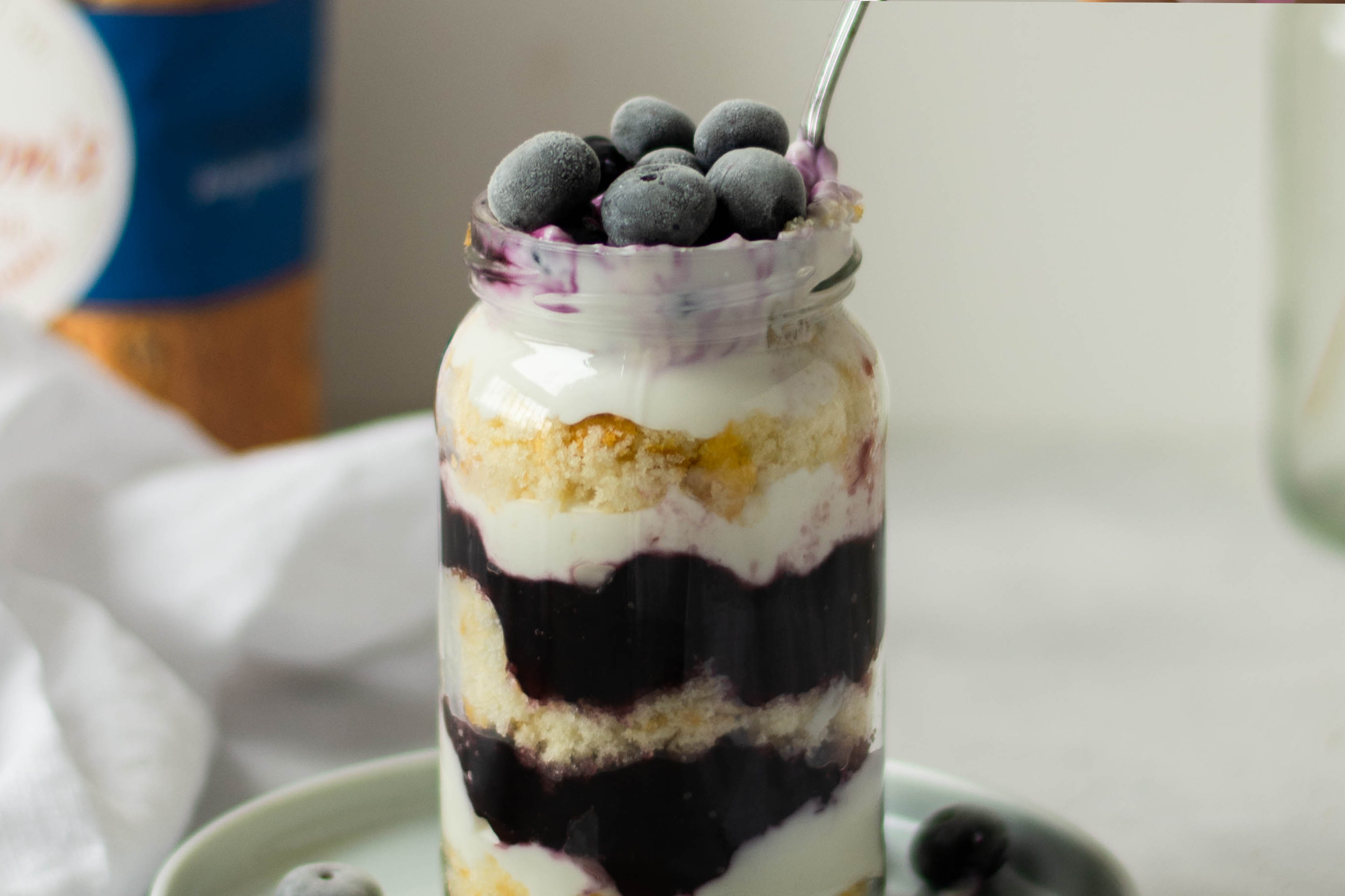 Close up of Lemon & Blueberry Cake Jar with blueberries on the top, with a spoon dipped in to take a mouthful