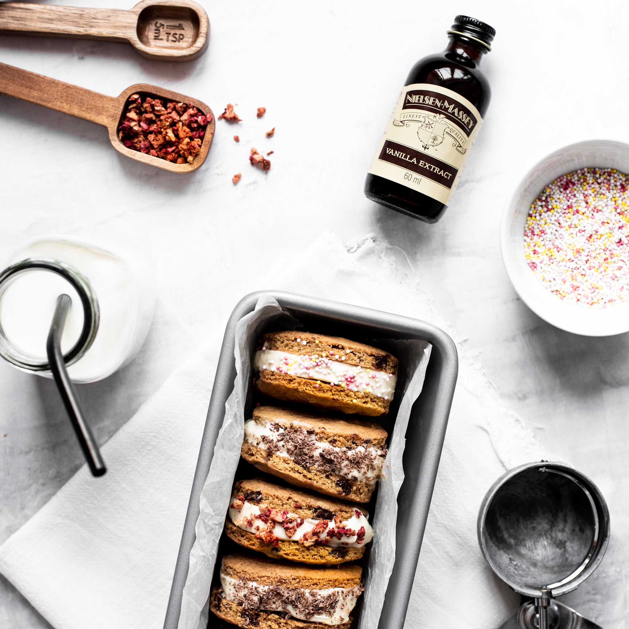 Set of four stuffed ice cream cookie sandwiches in a silver loaf tin next to an array of ingredients