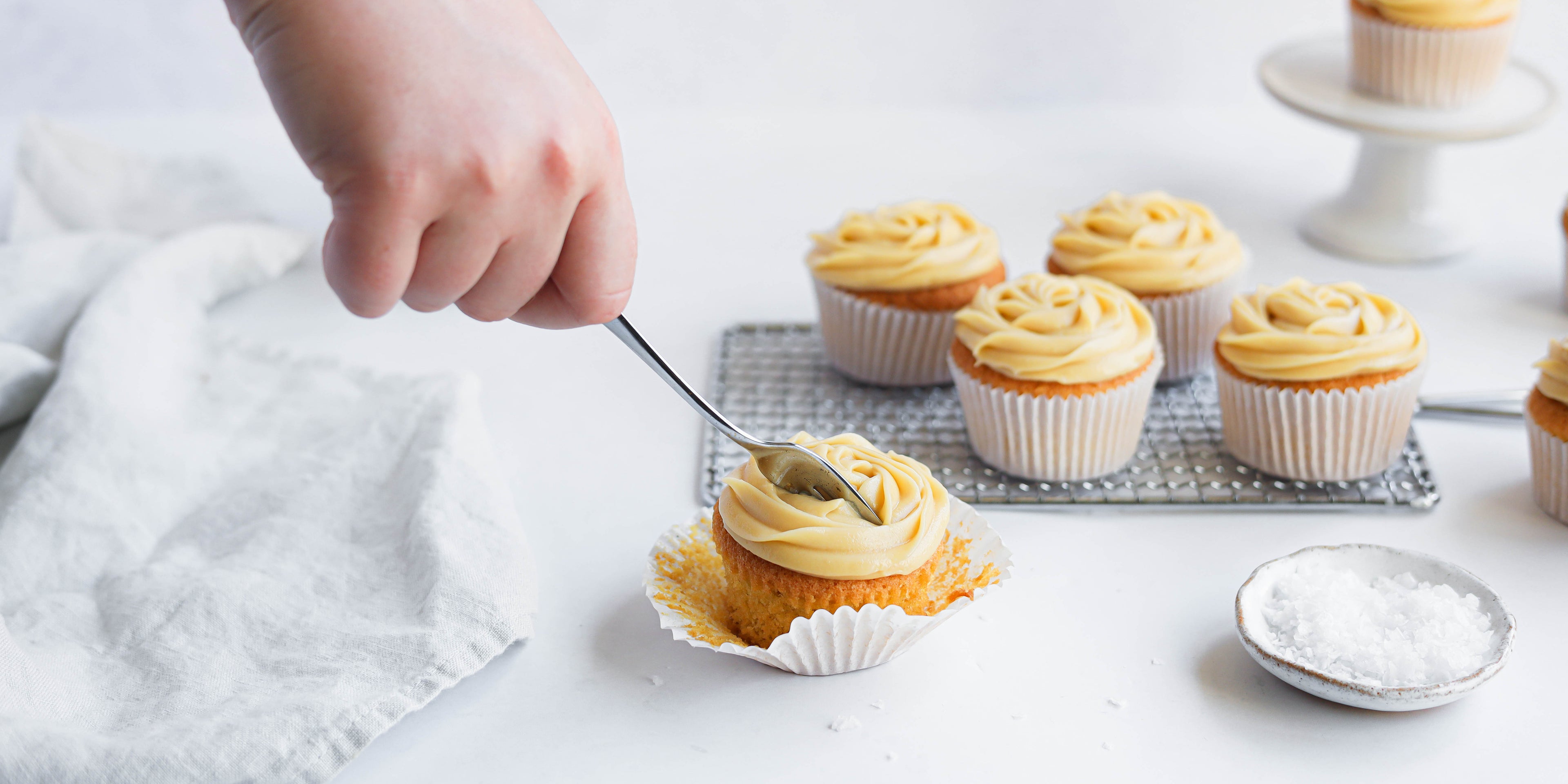 Salted Caramel Cupcakes with hand holding fork cutting into the cupcake buttercream, next to a small side dish of rock salt