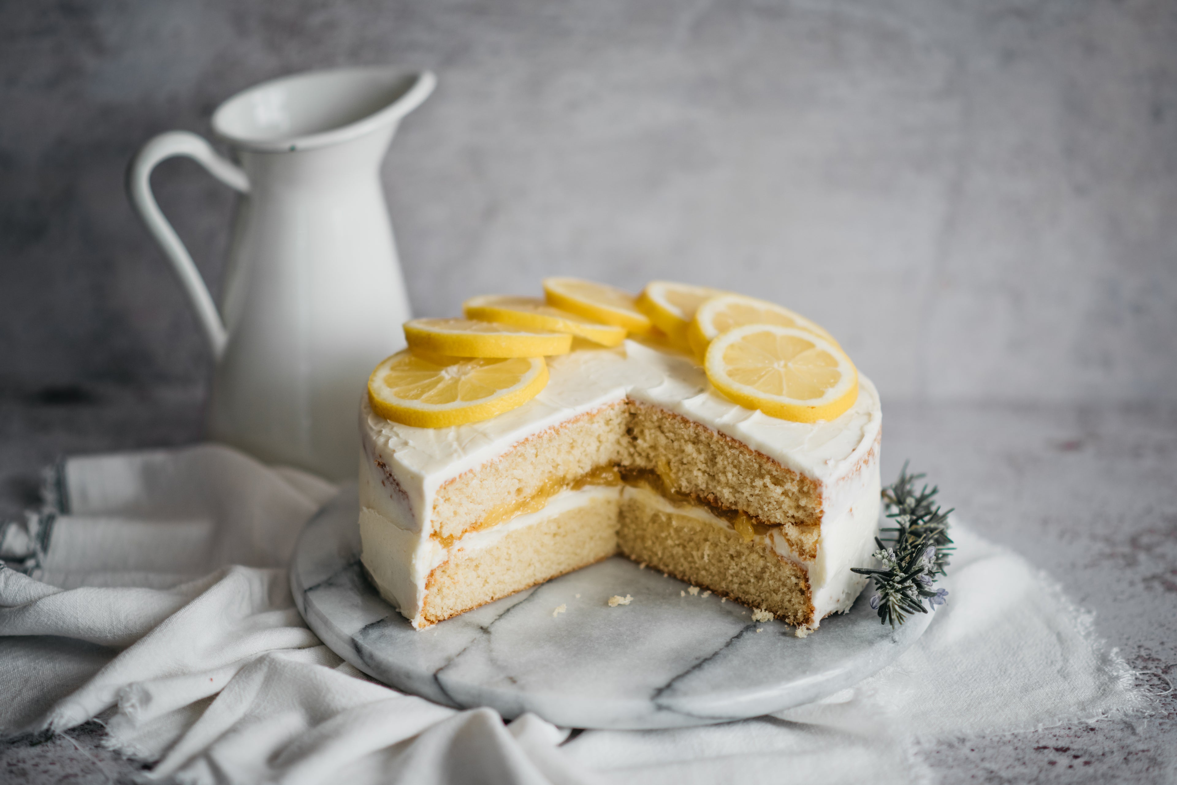 Gluten Free Elderflower & Lemon Cake with a slice cut out of it showing the lemon filled layers. Topped with slices of lemon