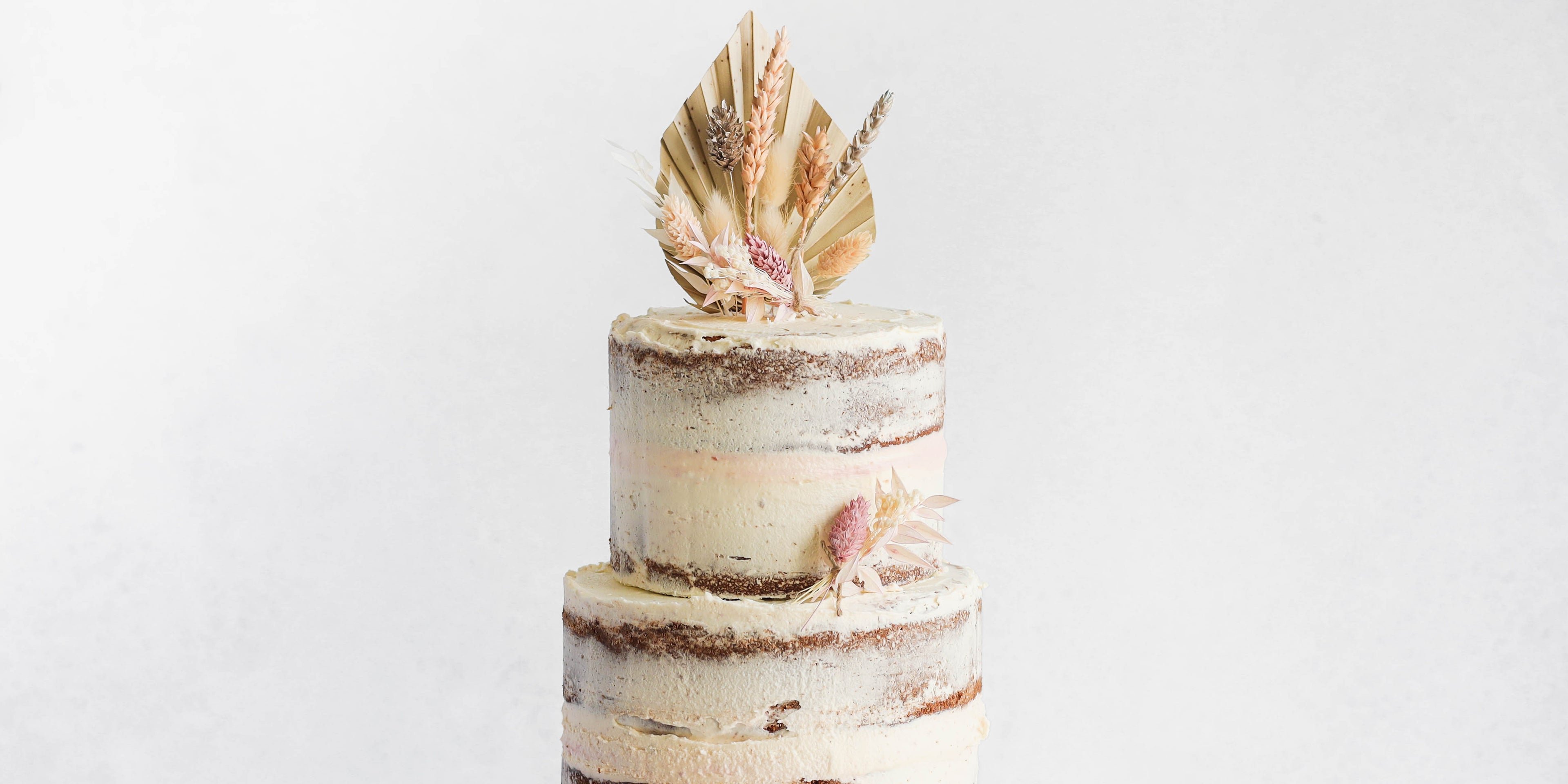 Close up view of a naked vanilla celebration cake topped with dried flowers