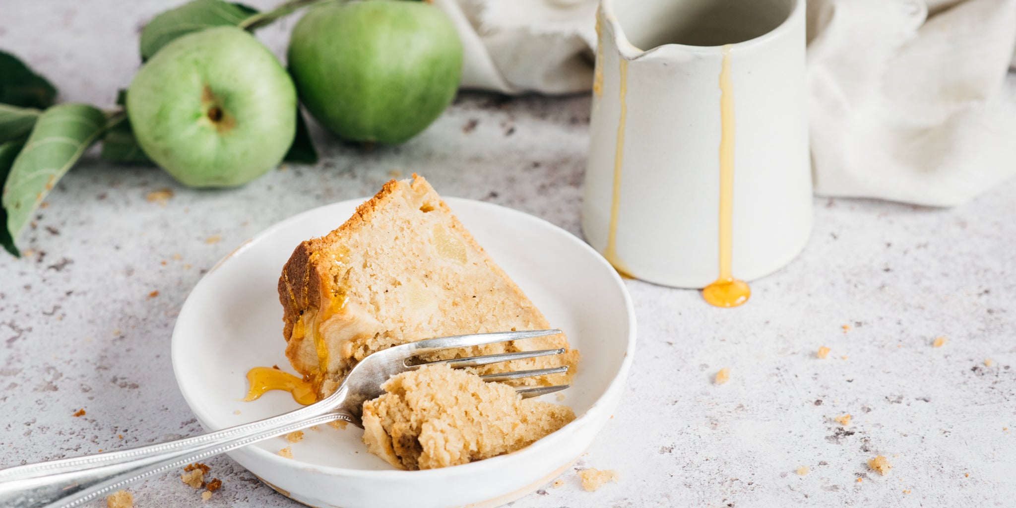 Slice of apple cake on plate with fork and jug in background