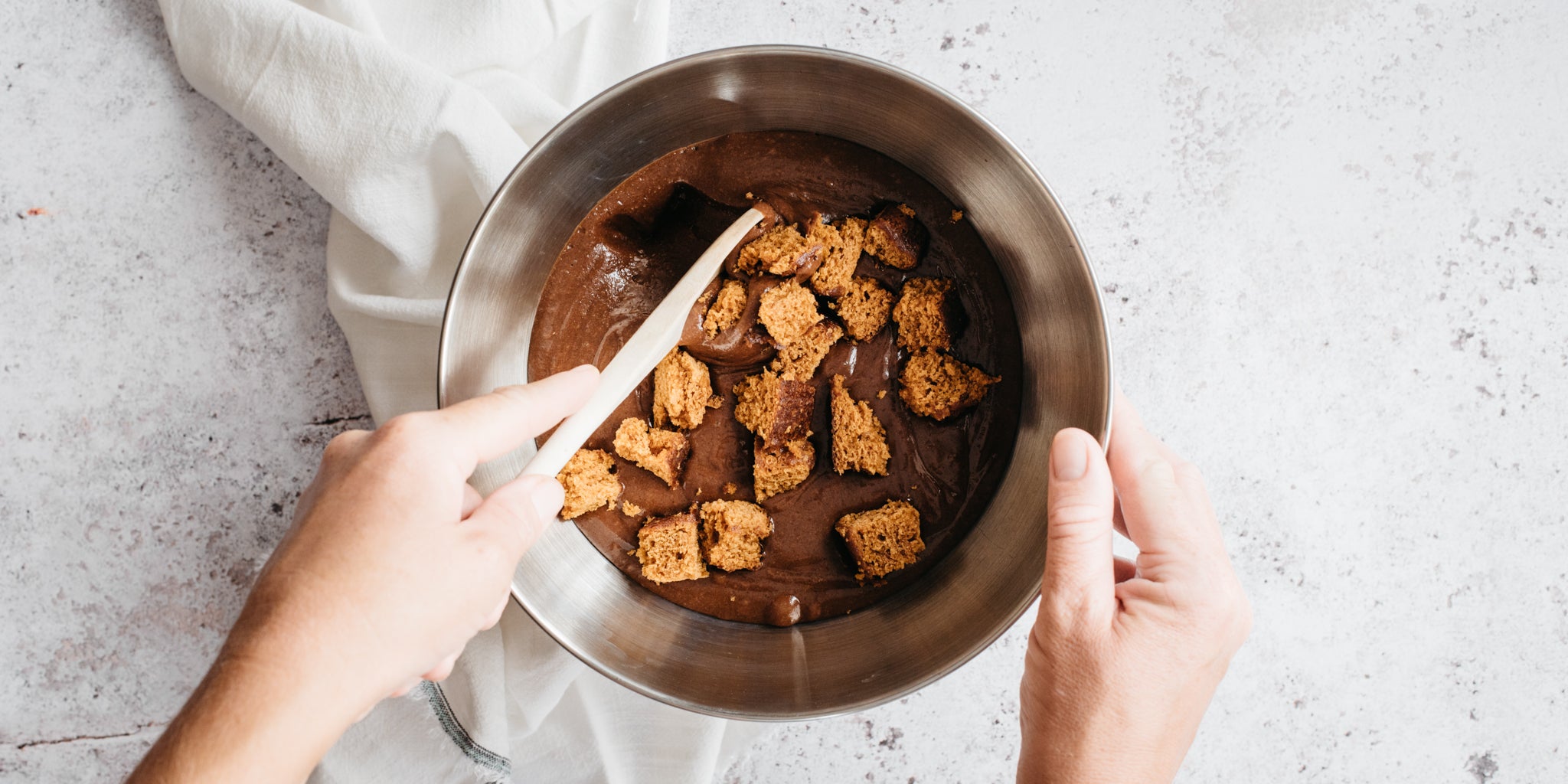 Metal bowl with hands stirring the chocolate mixture with a wooden spoon