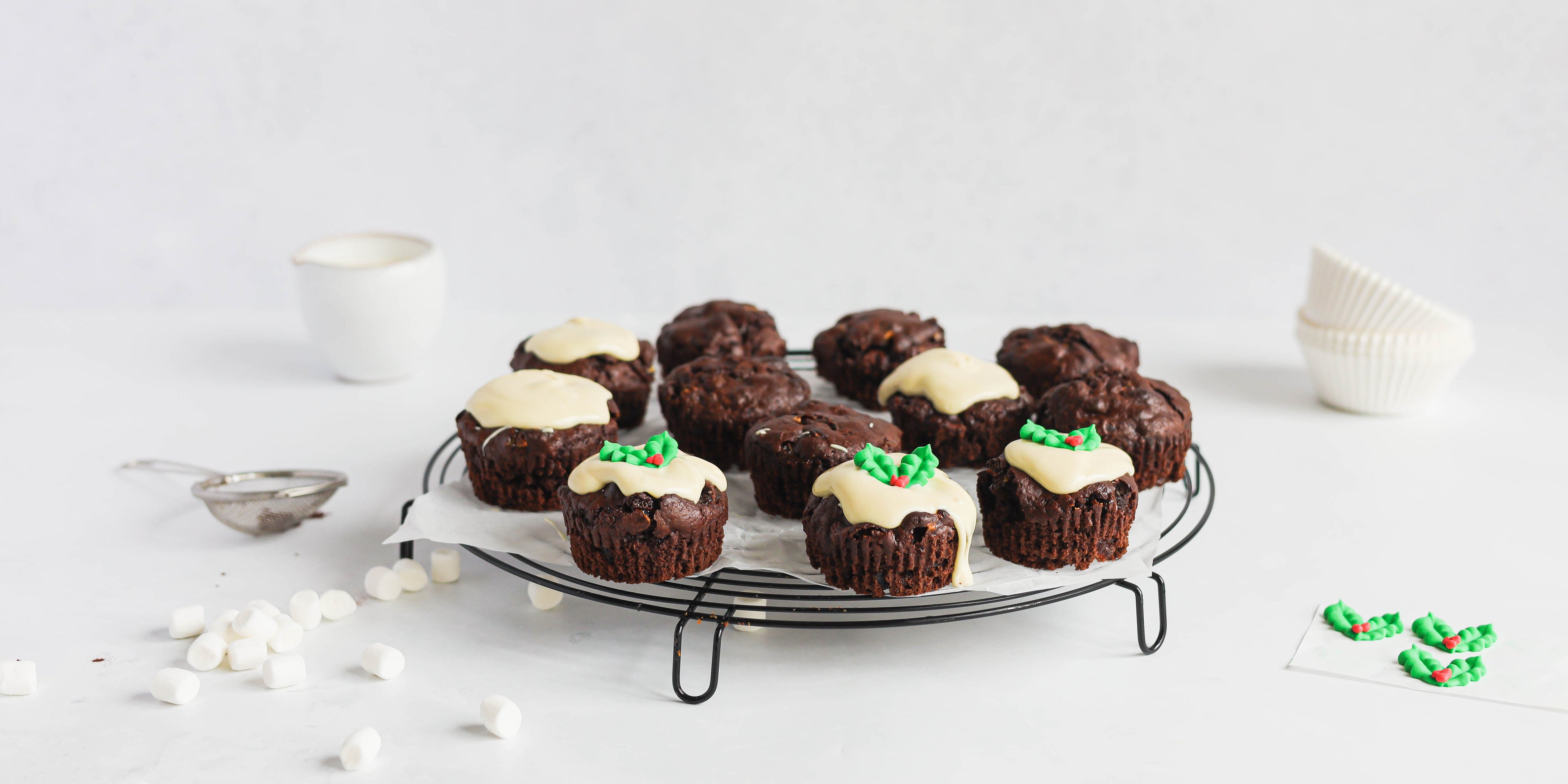 Mini Rocky Road Christmas Pudding Muffins on a wire rack, being decorated with white chocolate and holly.