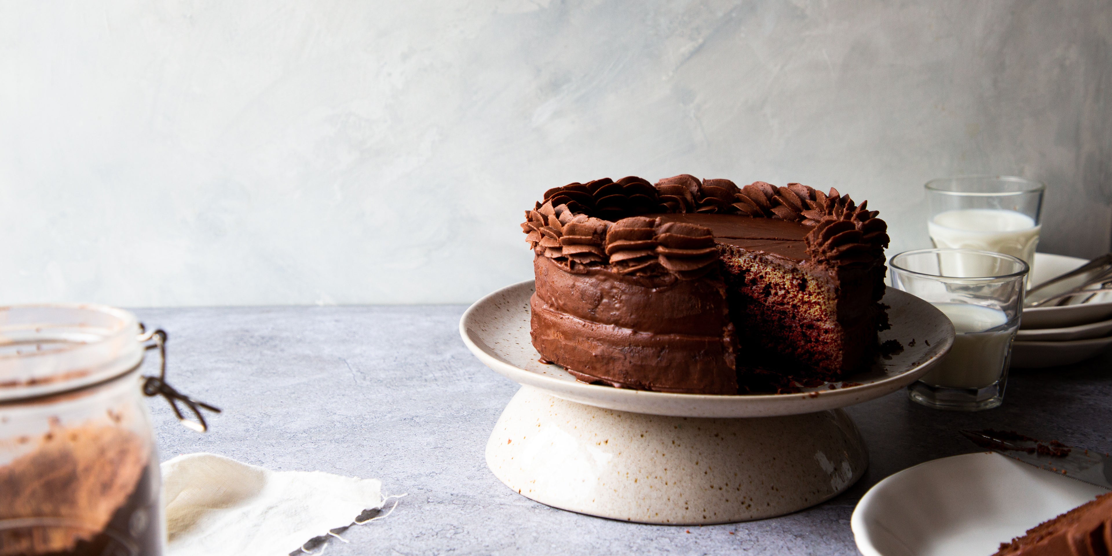 Classic Chocolate Cake on a cake stand with a slice cut out of it showing the rich layers inside