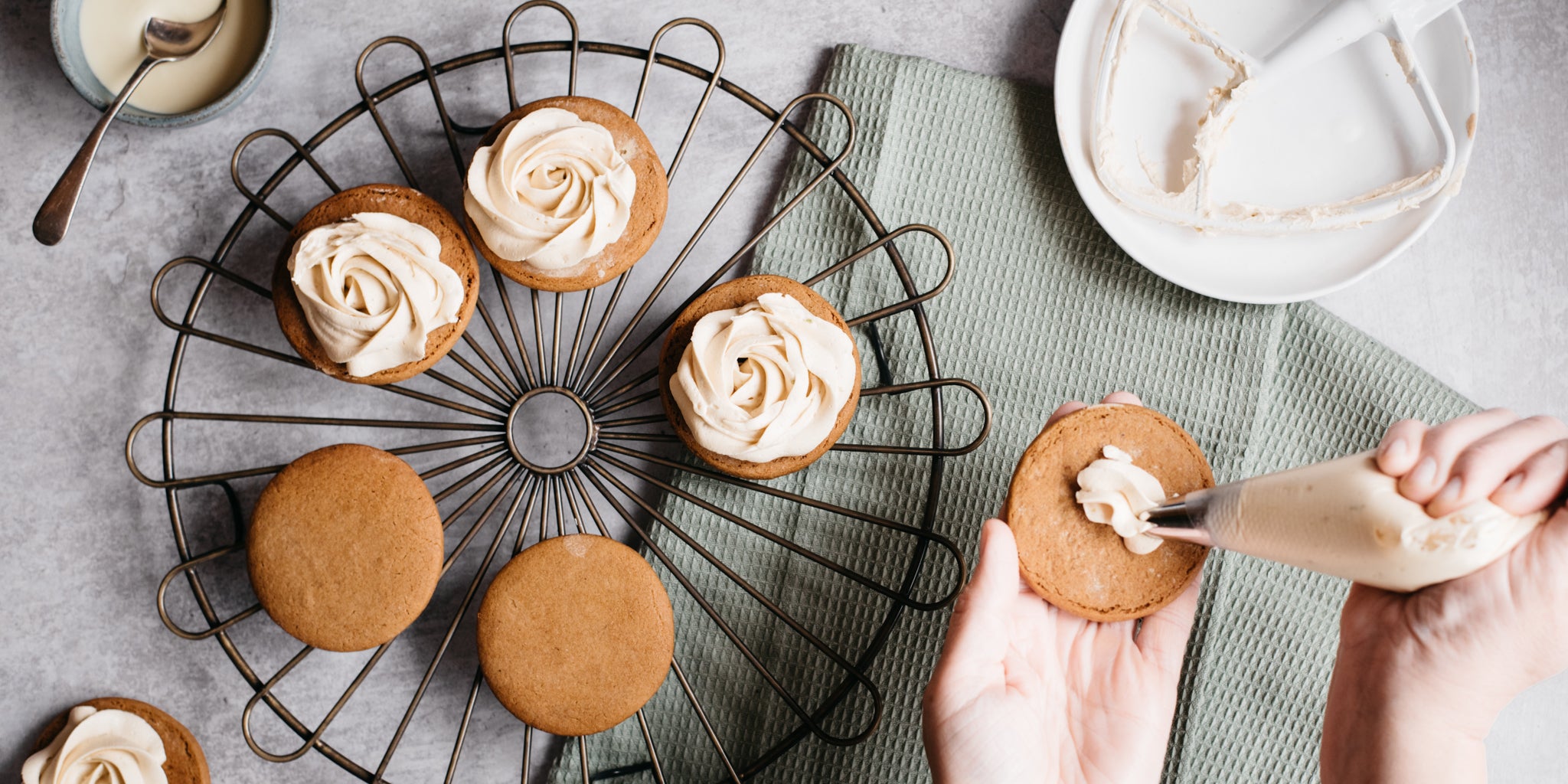 Citrus Gingerbread Cookies being hand piped with plant based lime buttercream filling, on a wire cooling rack.