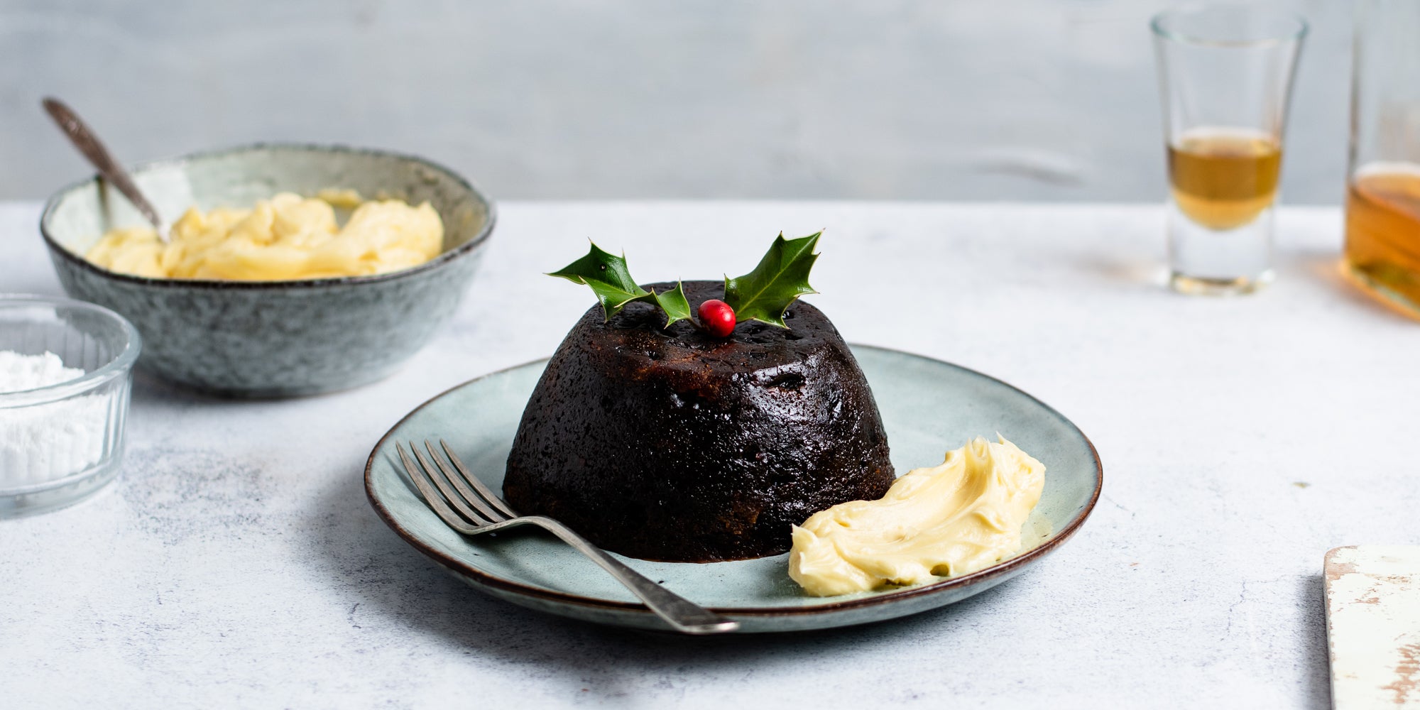 Brandy Butter on a plate next to a Christmas pudding. Glass of brandy in the background