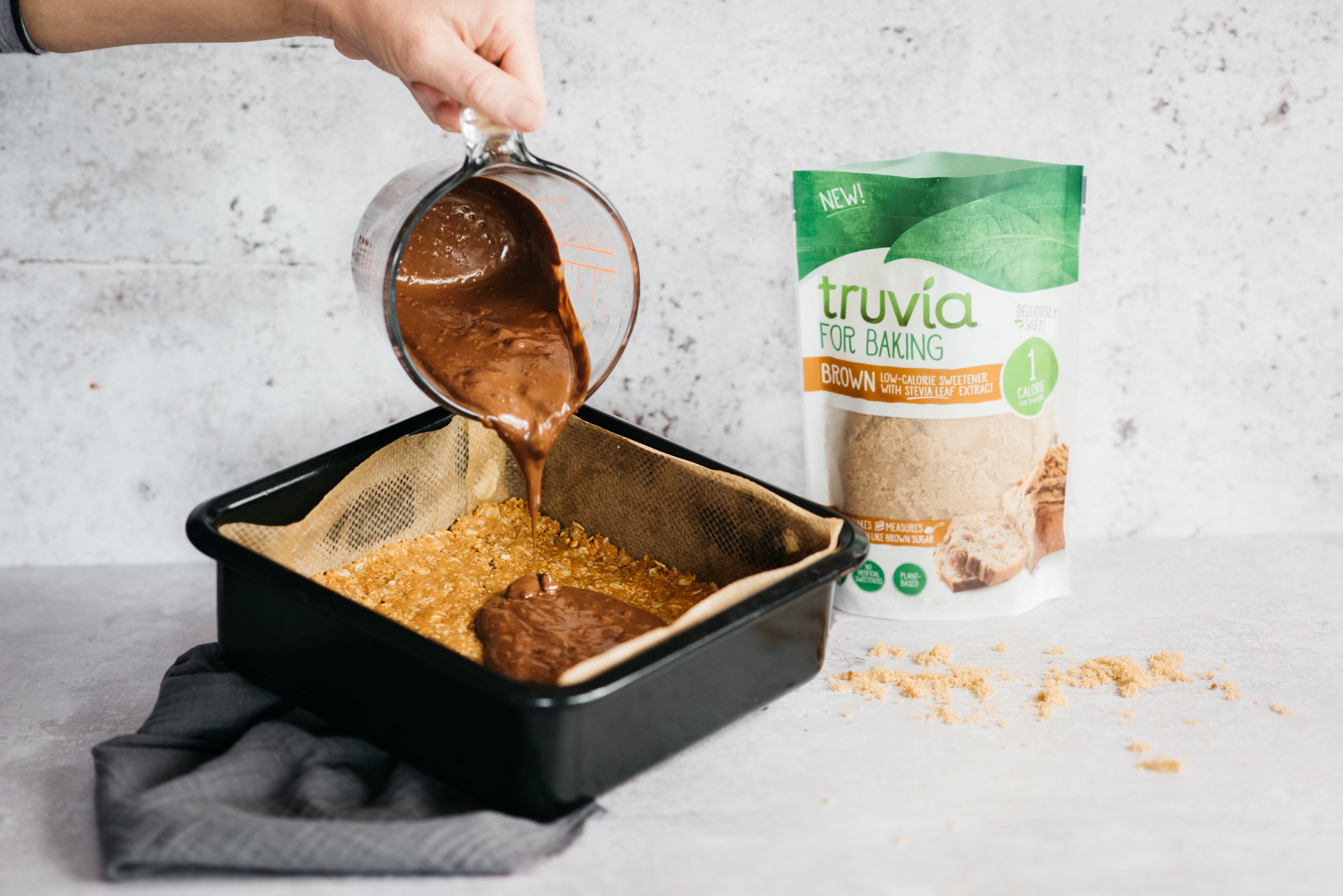 Melted chocolate being poured onto a oat based, next to a bag of Truvia for Baking Brown